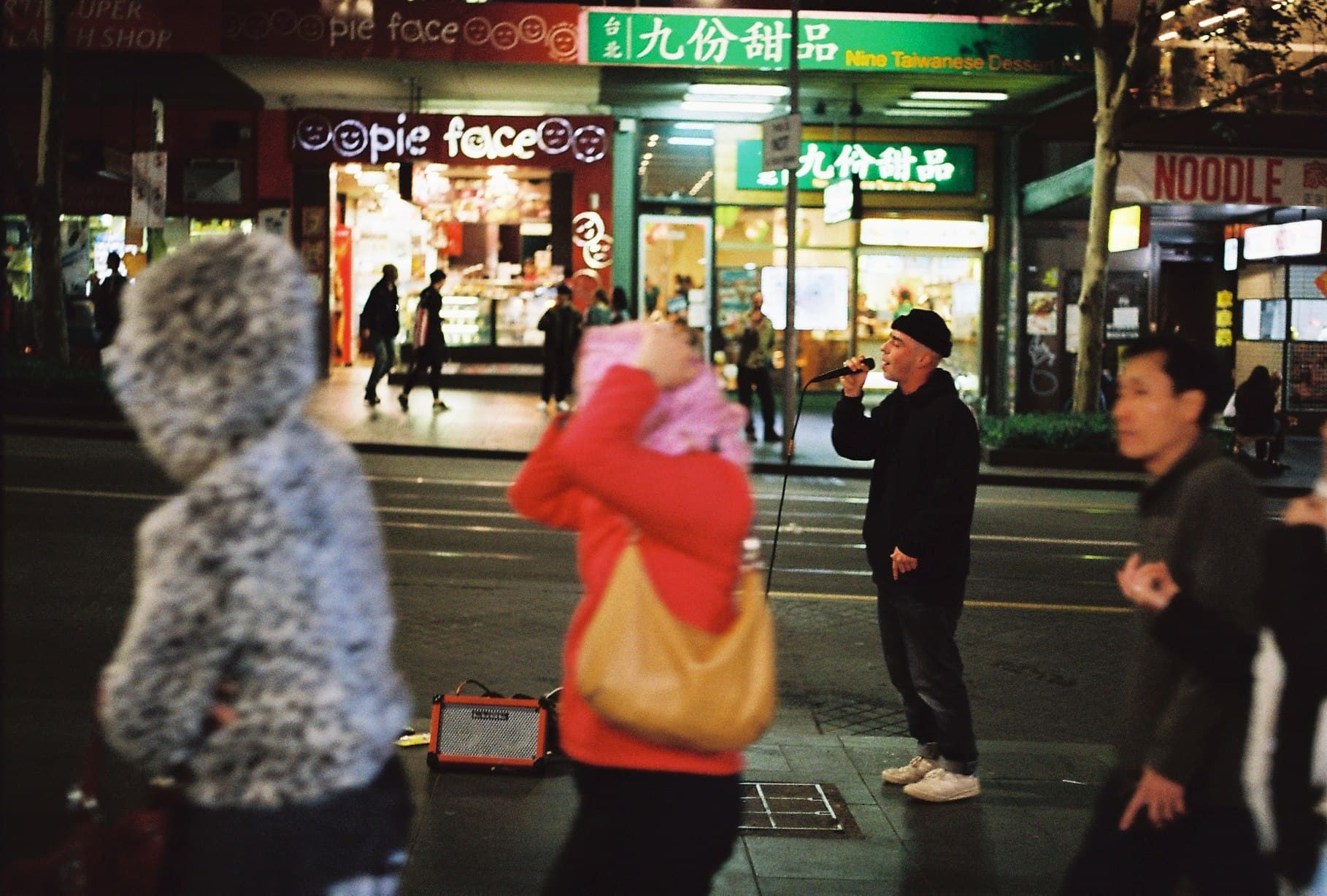 People gathered outside a brightly lit shop at night.