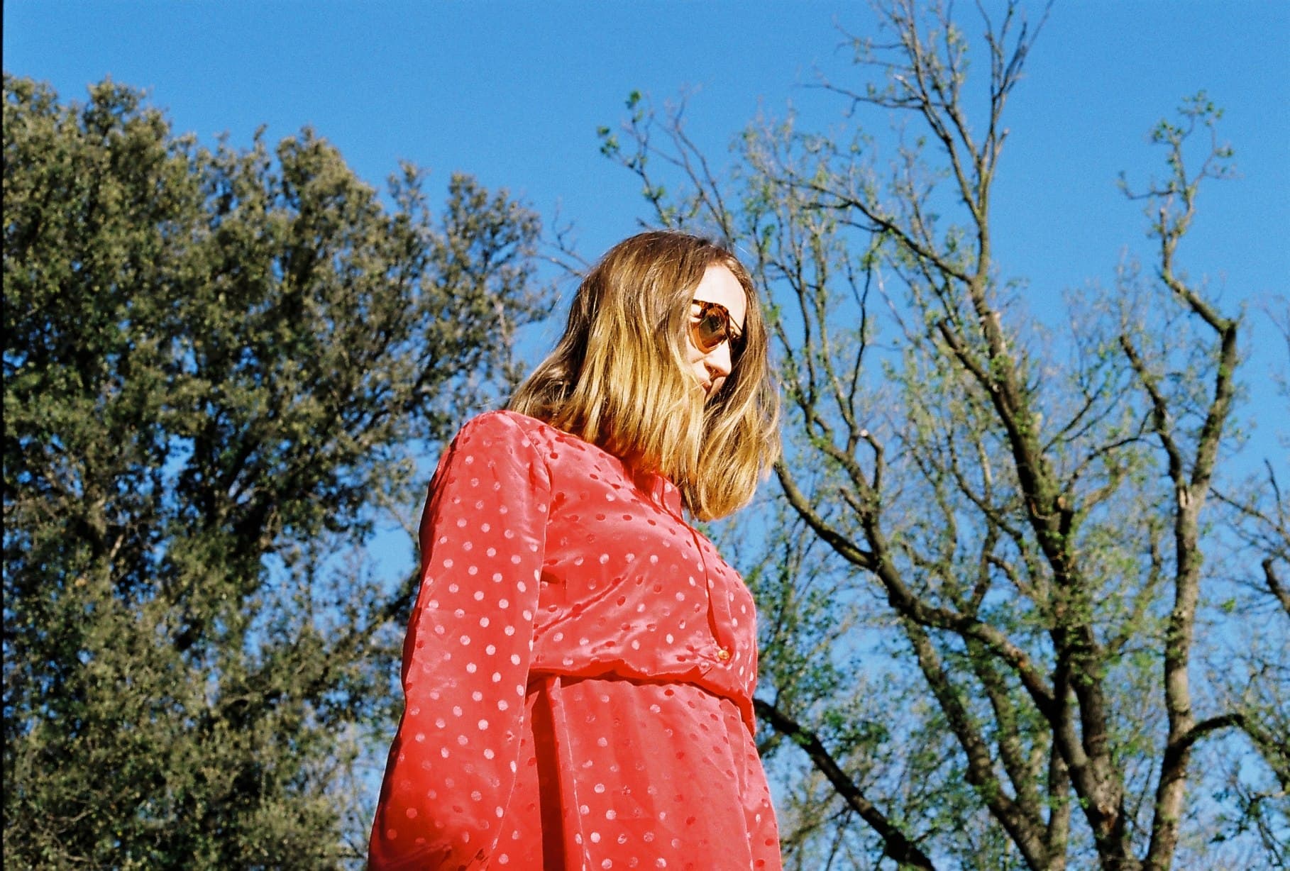 A person in a red patterned shirt beneath trees.