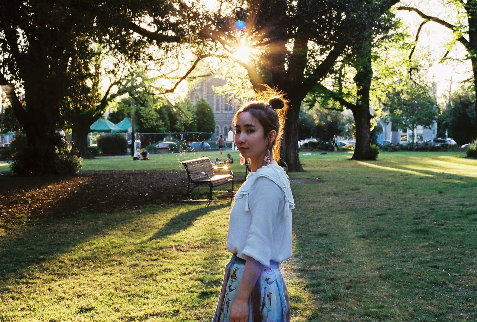 Portrait in a sunlit park beneath leafy trees.