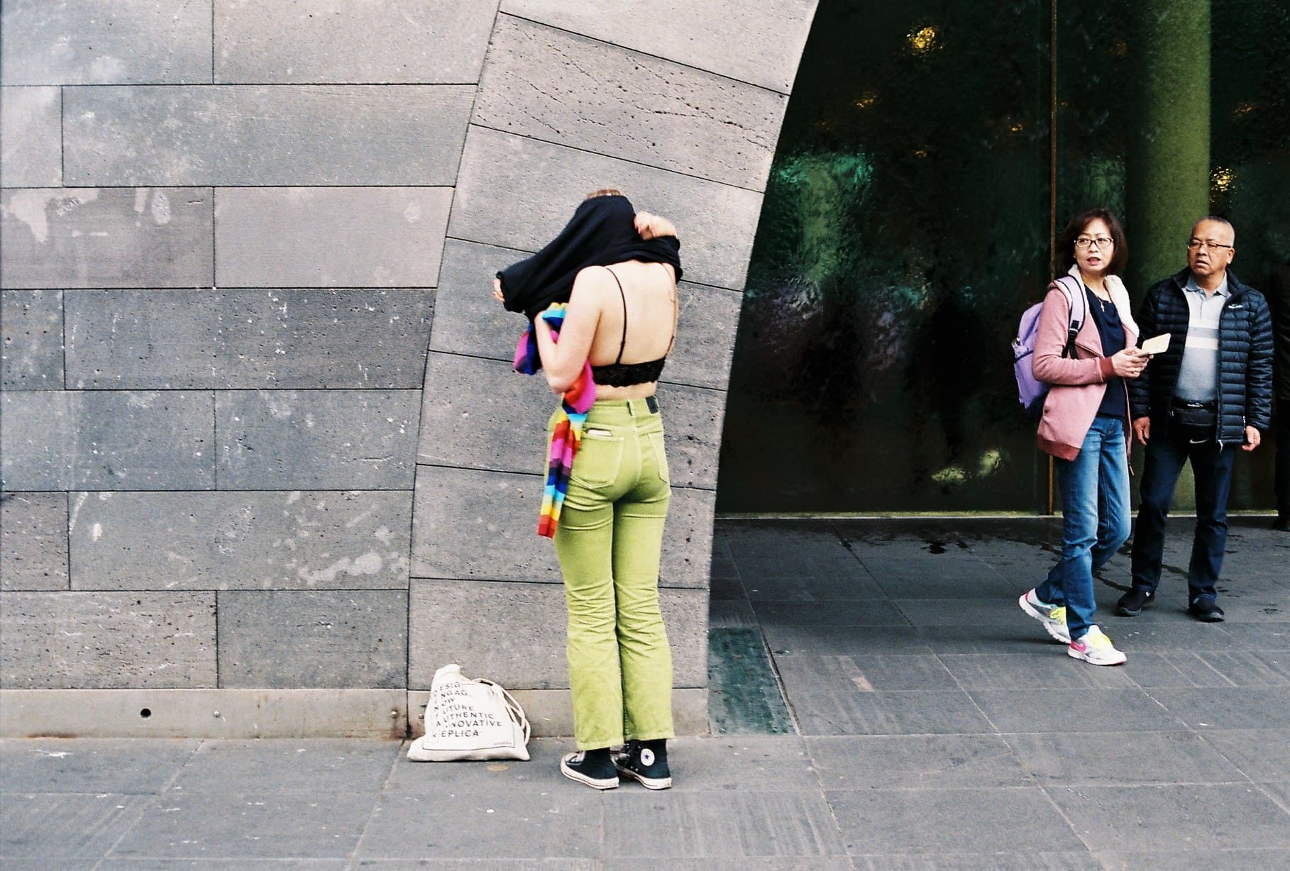 A person in green trousers beside a stone building.