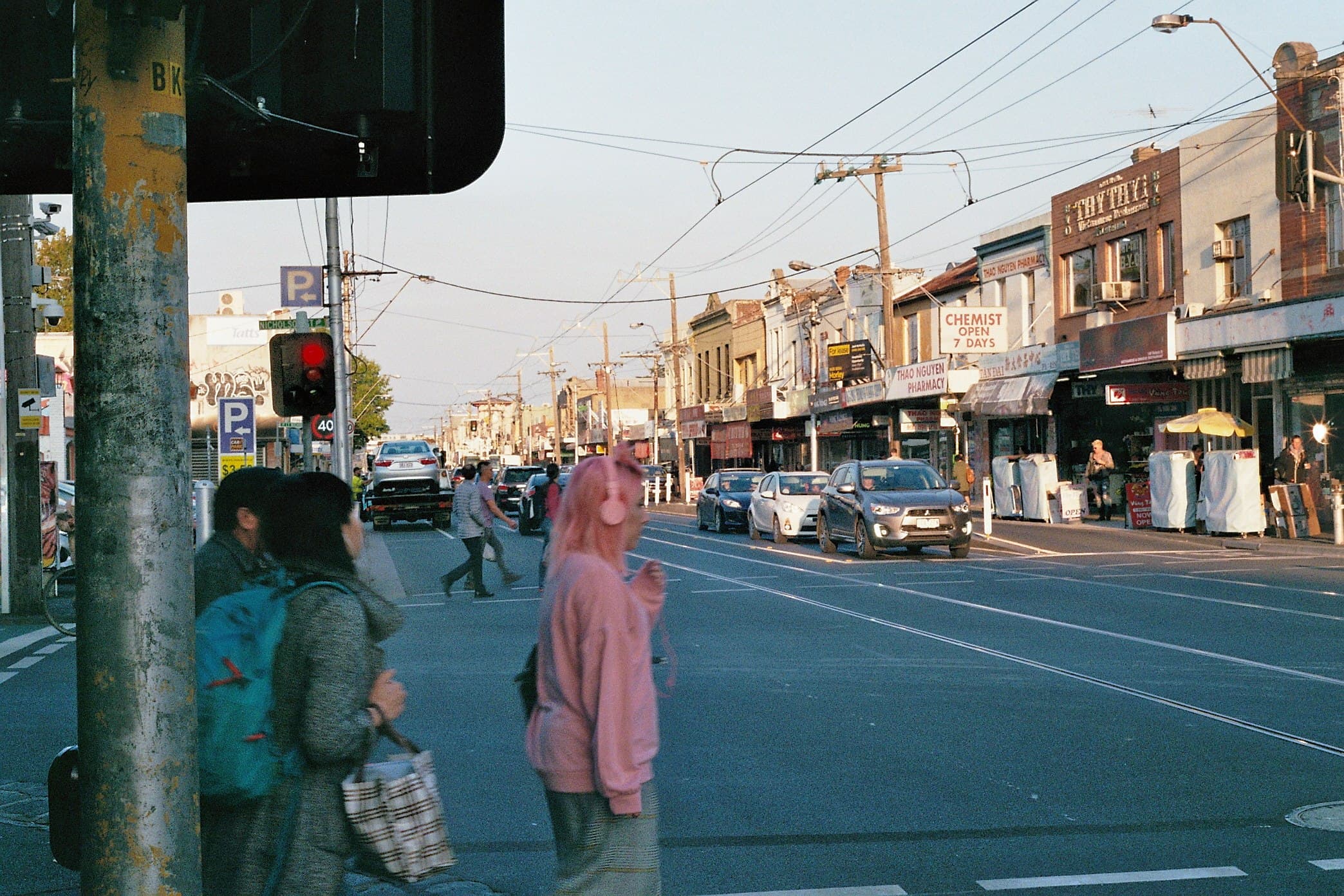 Pedestrians crossing a sunlit city street.