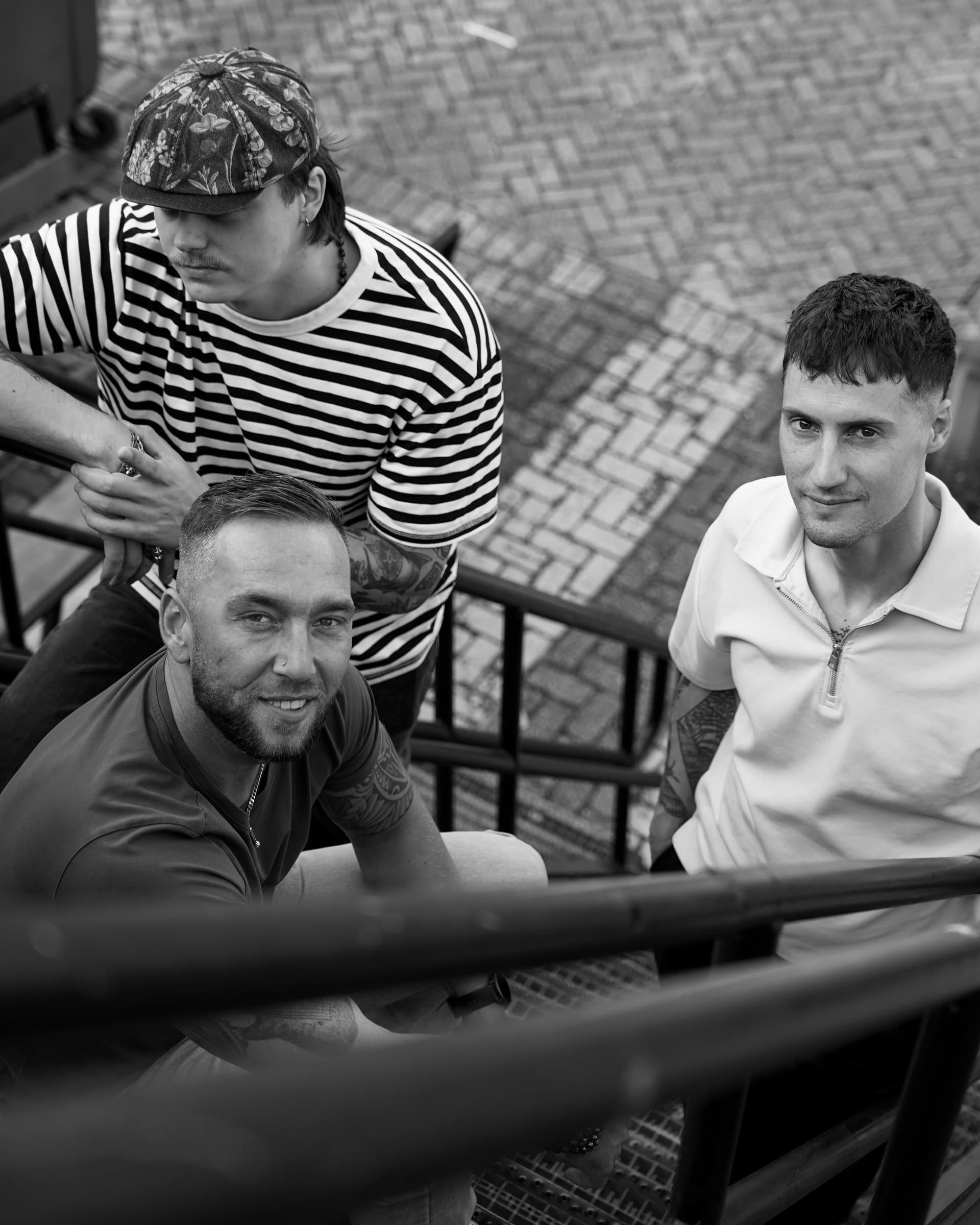 Black-and-white portrait of the three Corleone band members on a metal staircase, seen from above.