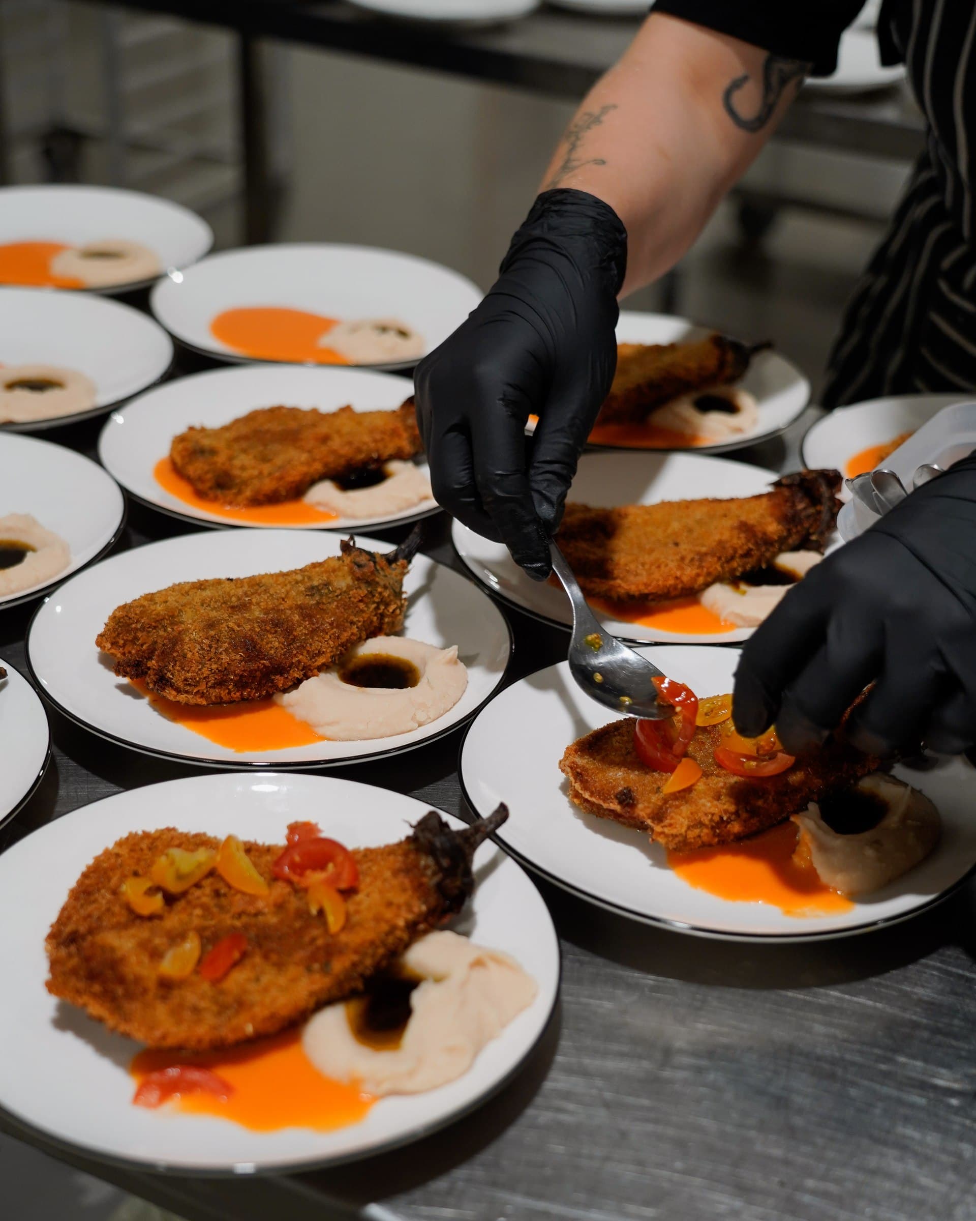 Gloved hands plating food for a De Groentemans pop-up dinner.