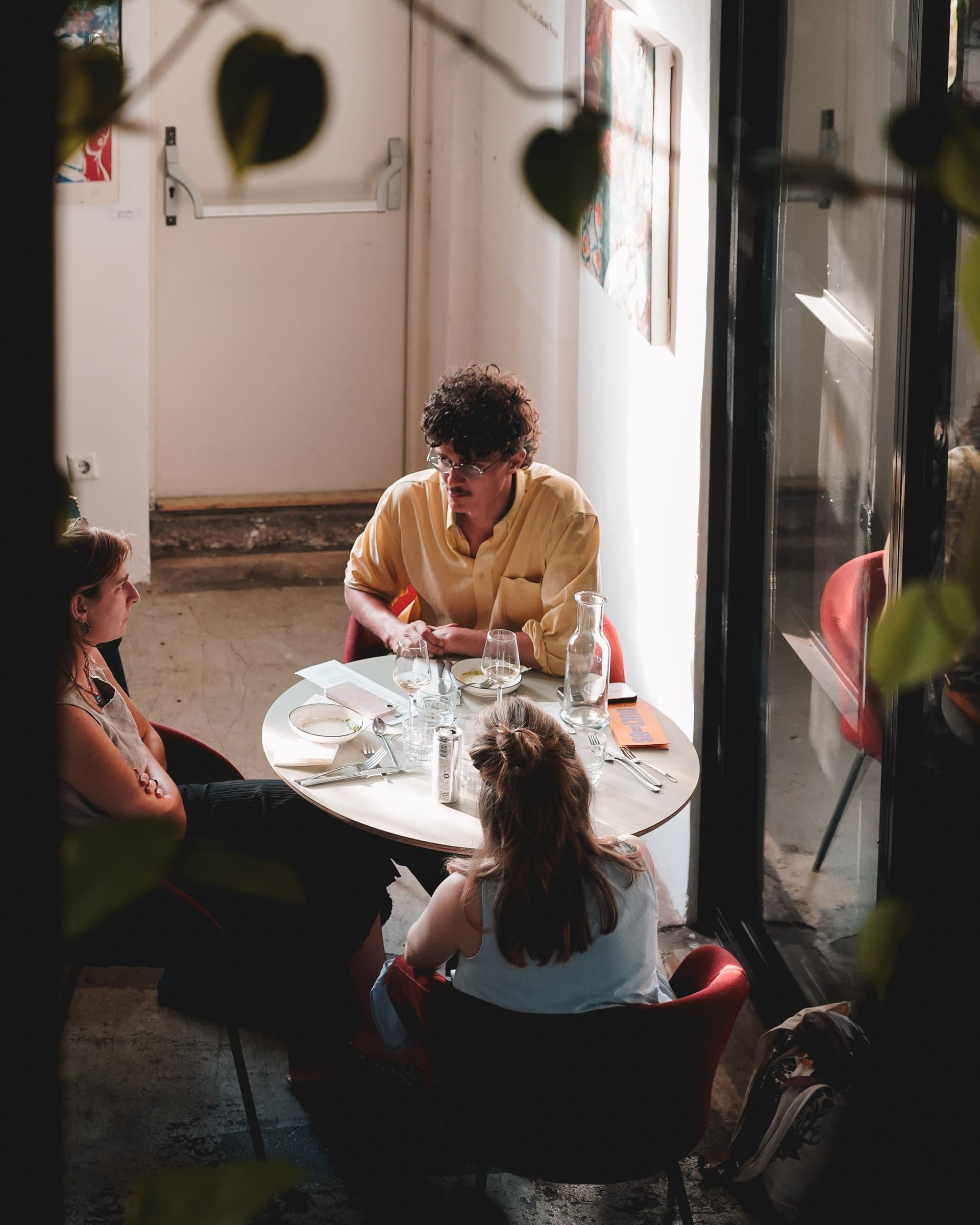 Guests gathered around a small table beside a sunlit window.