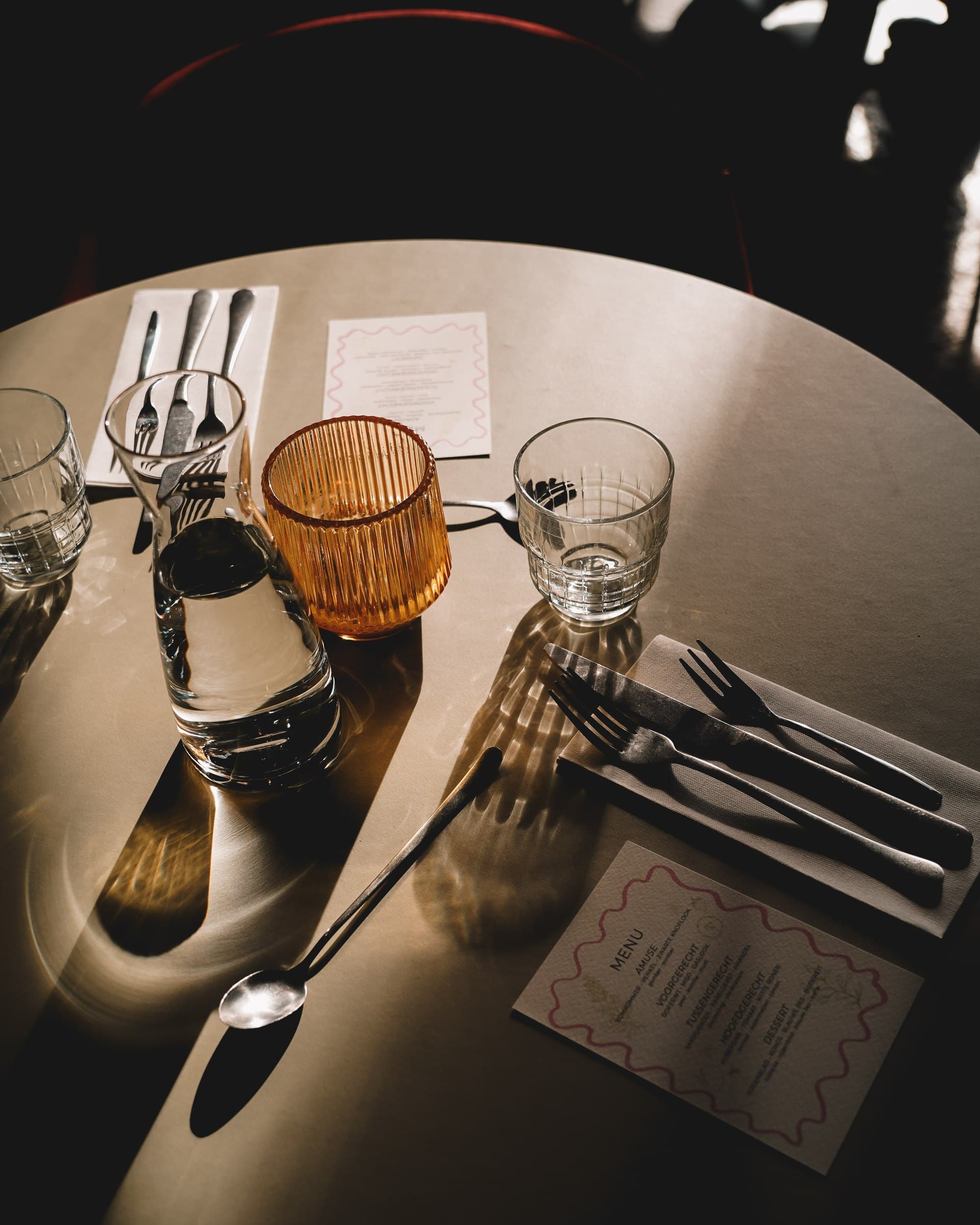 Cutlery, glasses and a printed menu on a sunlit table.