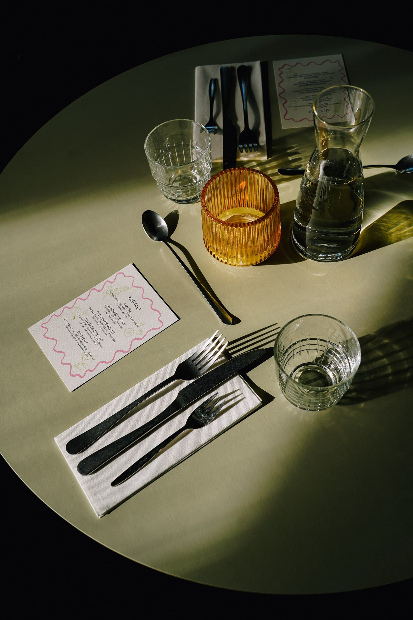 A table setting with cutlery, menu and an amber drinking glass.