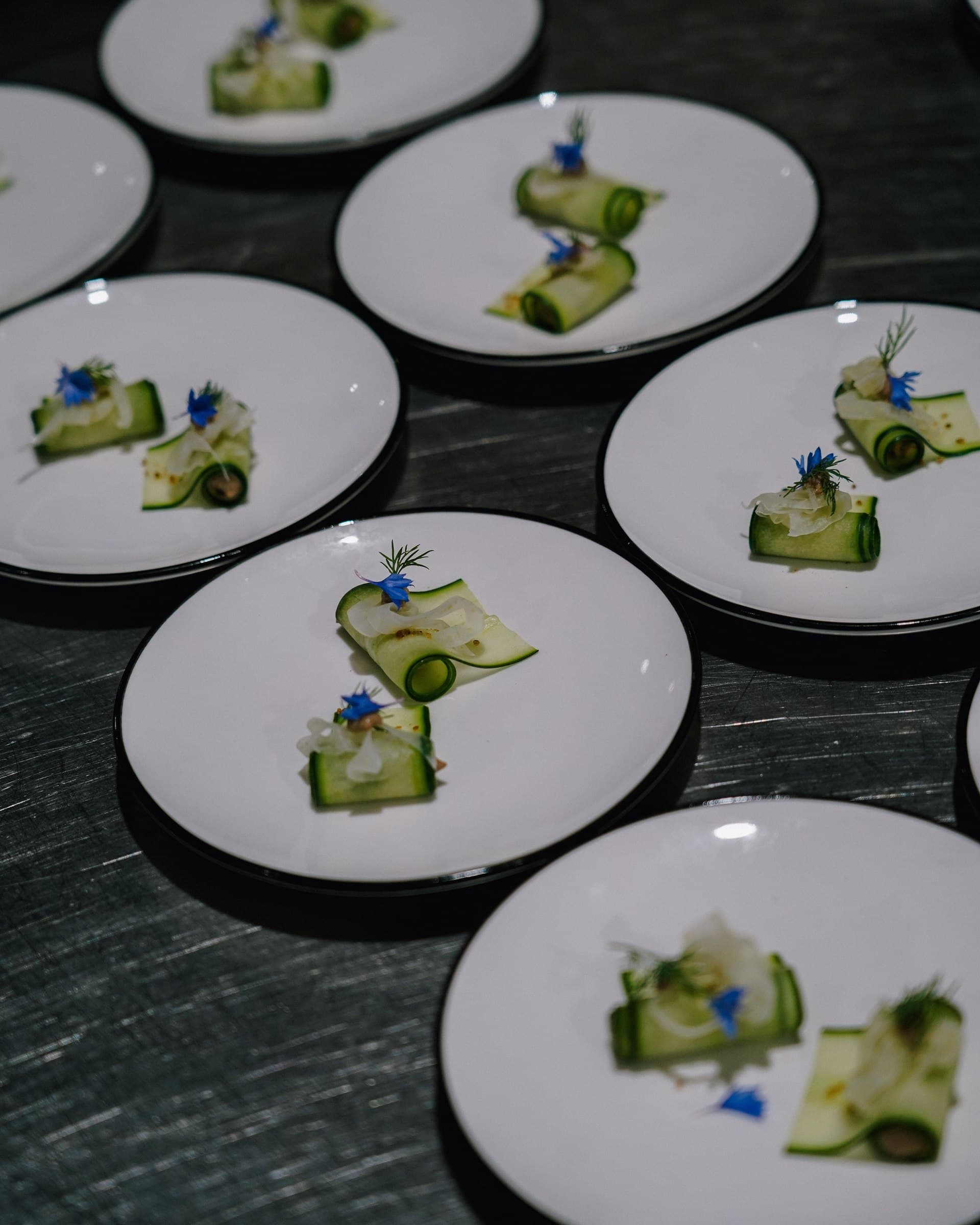 Rows of white plates with carefully arranged green garnishes.