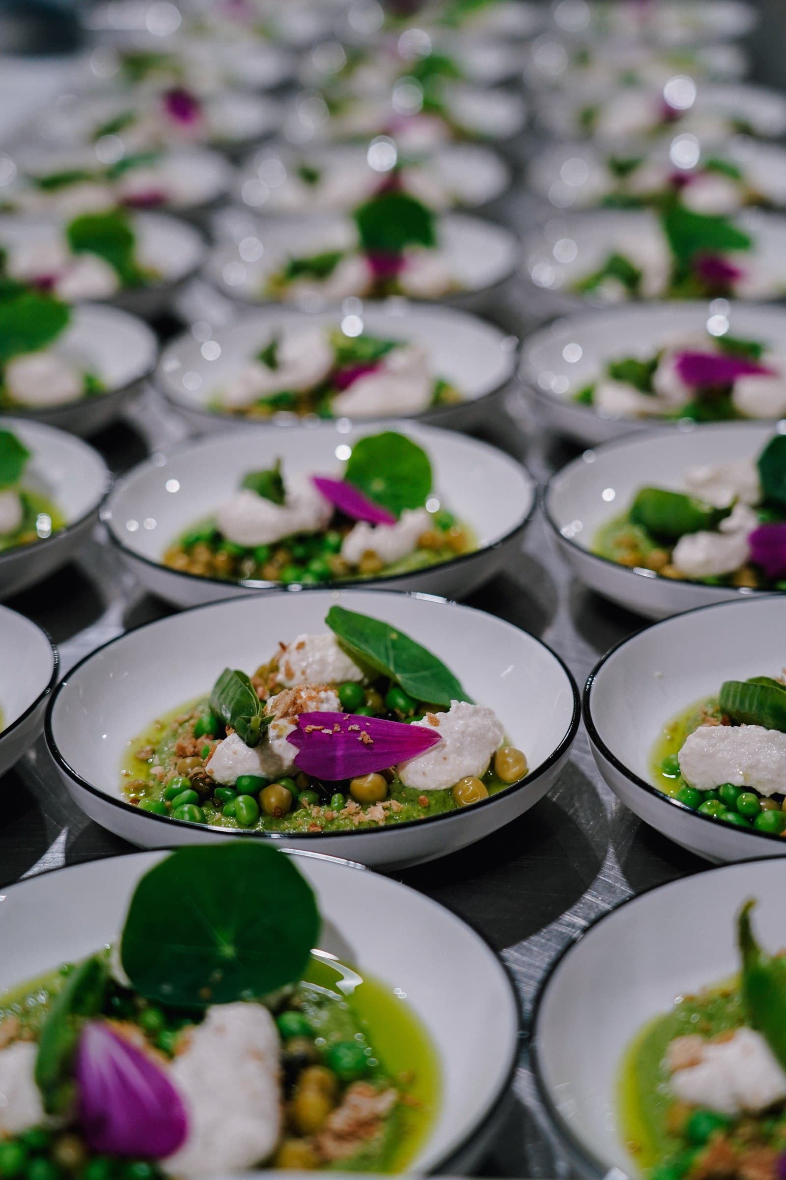 Plated dishes with vegetables and purple flowers, ready for service.