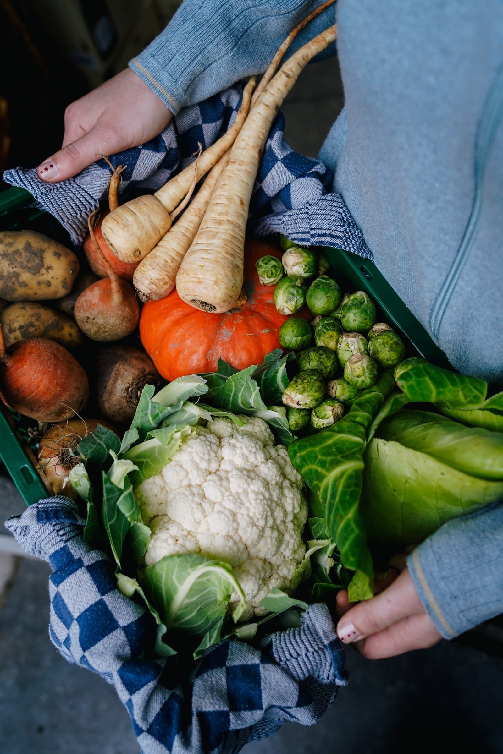 Hands preparing artichokes among fresh vegetables.
