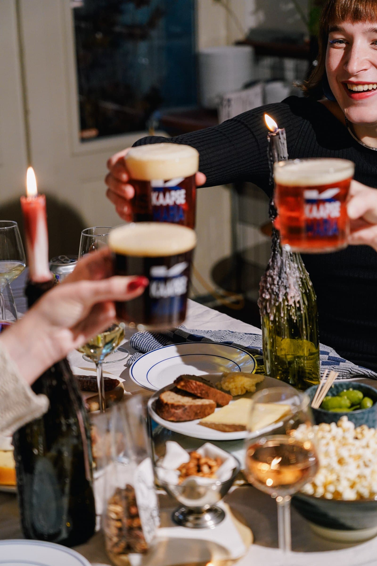 Hands raising beer glasses over a table of food.