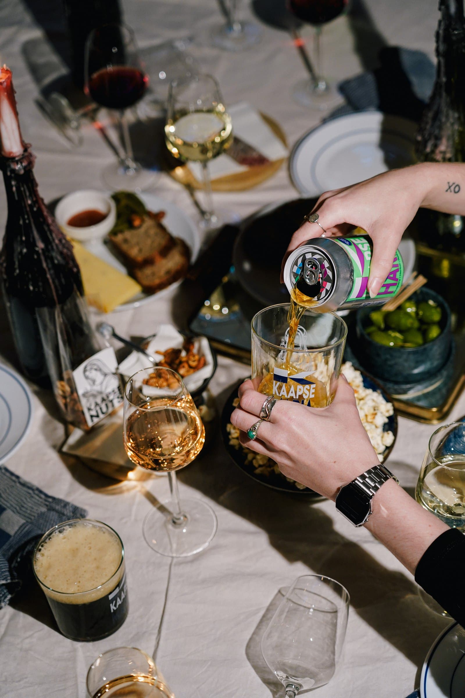 Hands pouring drinks around a table of shared food.