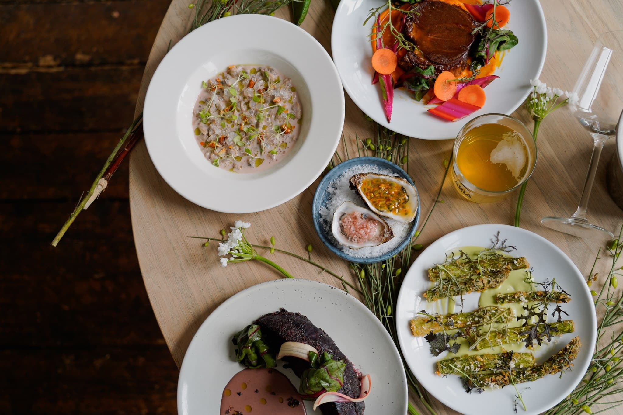 An overhead spread of several dishes, drinks and cutlery on a wooden table.