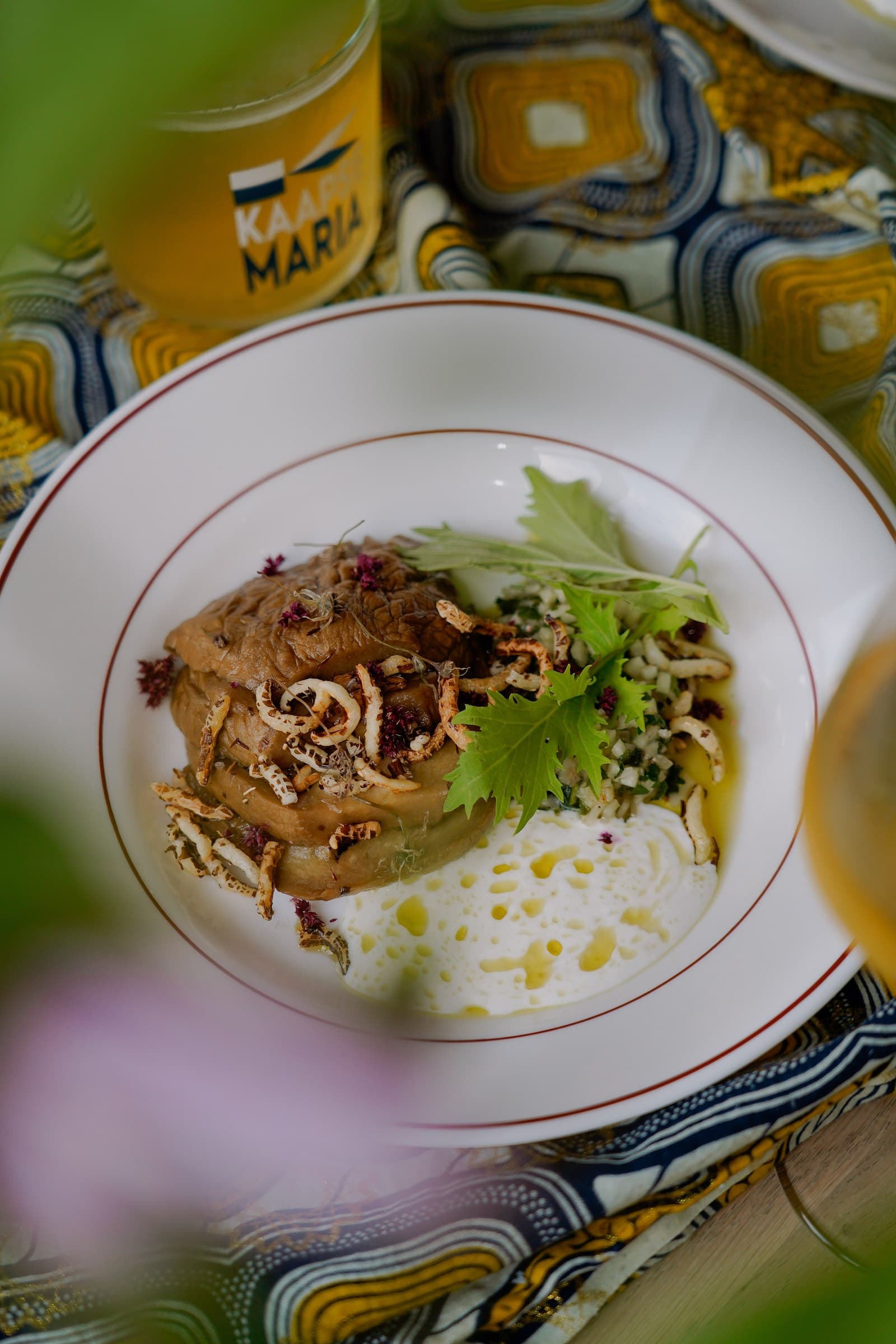 A plated dish with noodles and vegetables on a patterned tablecloth.