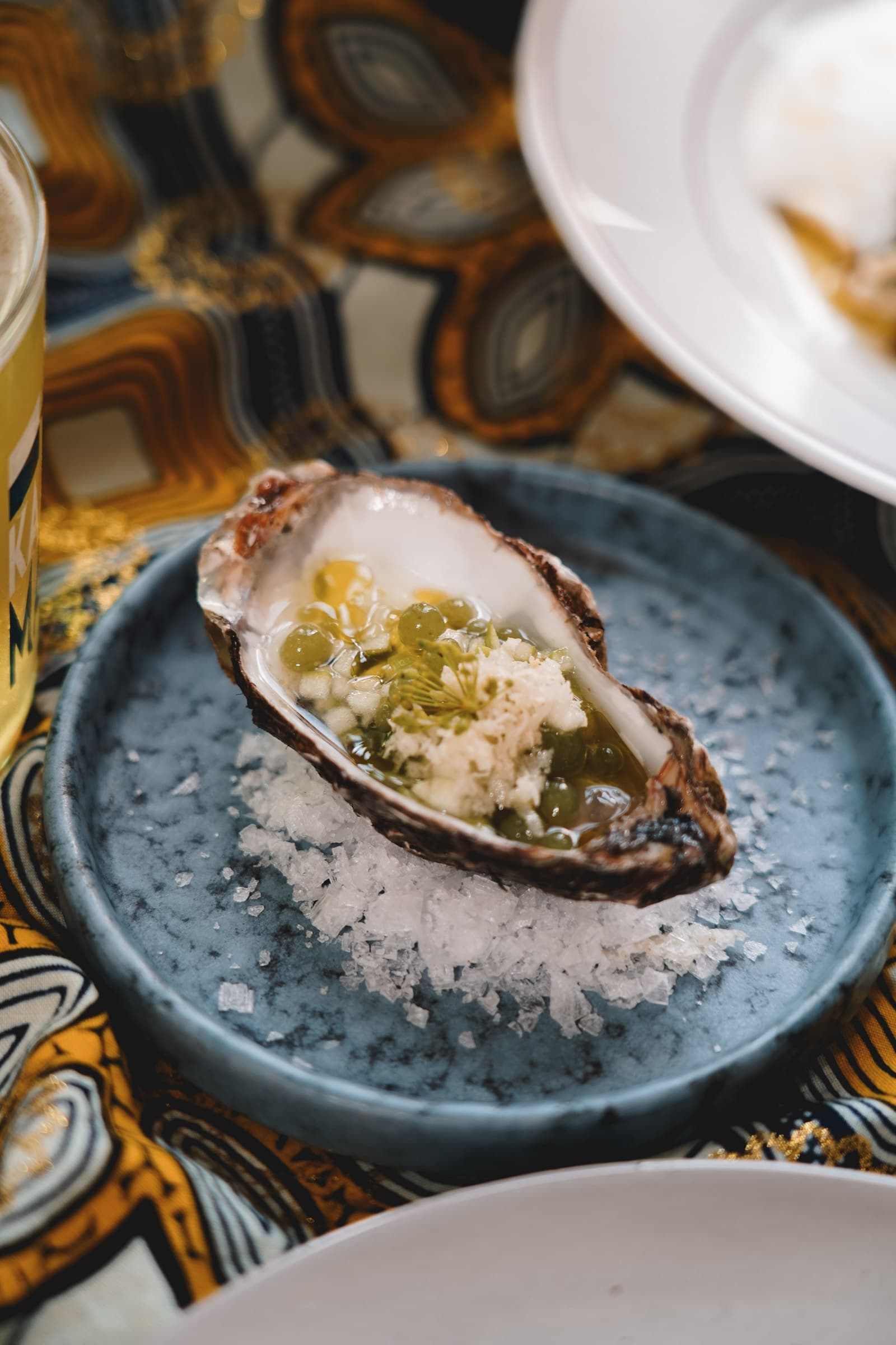 A shellfish dish on a blue plate beside drinks and tableware.