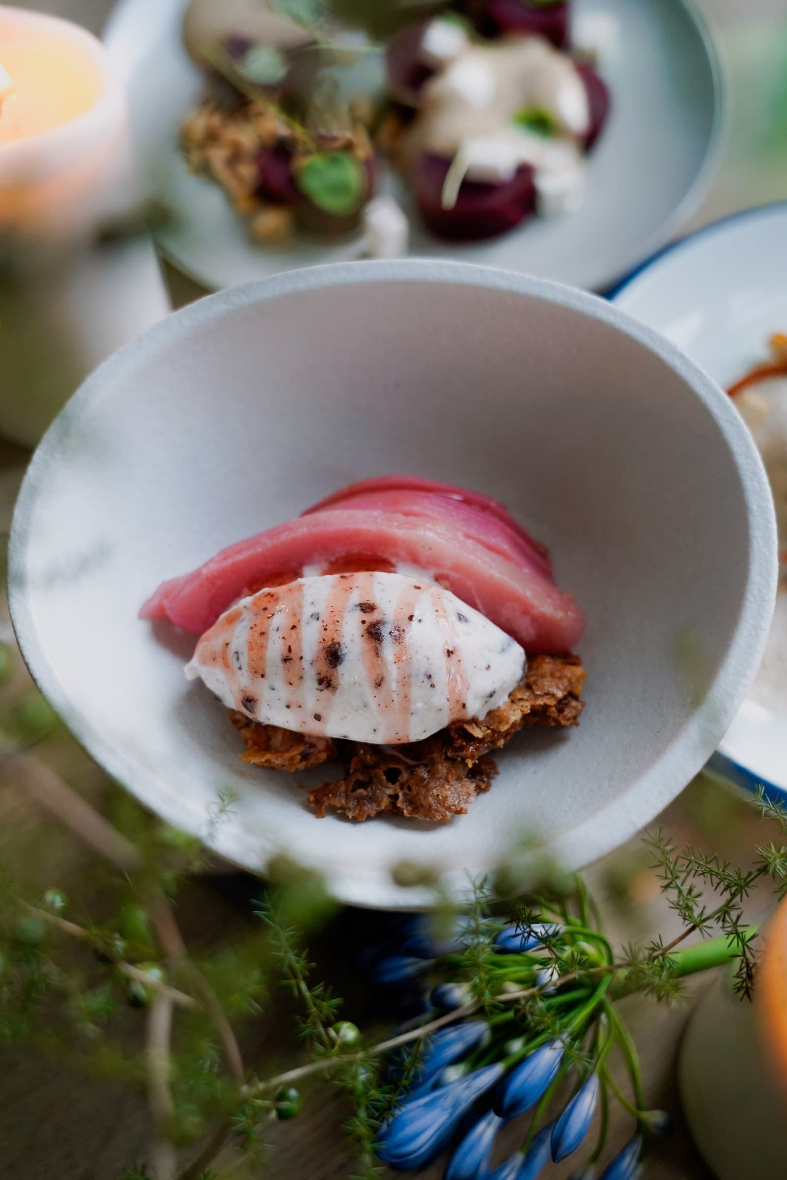 A pink-toned dish on a white plate with green leaves in the foreground.