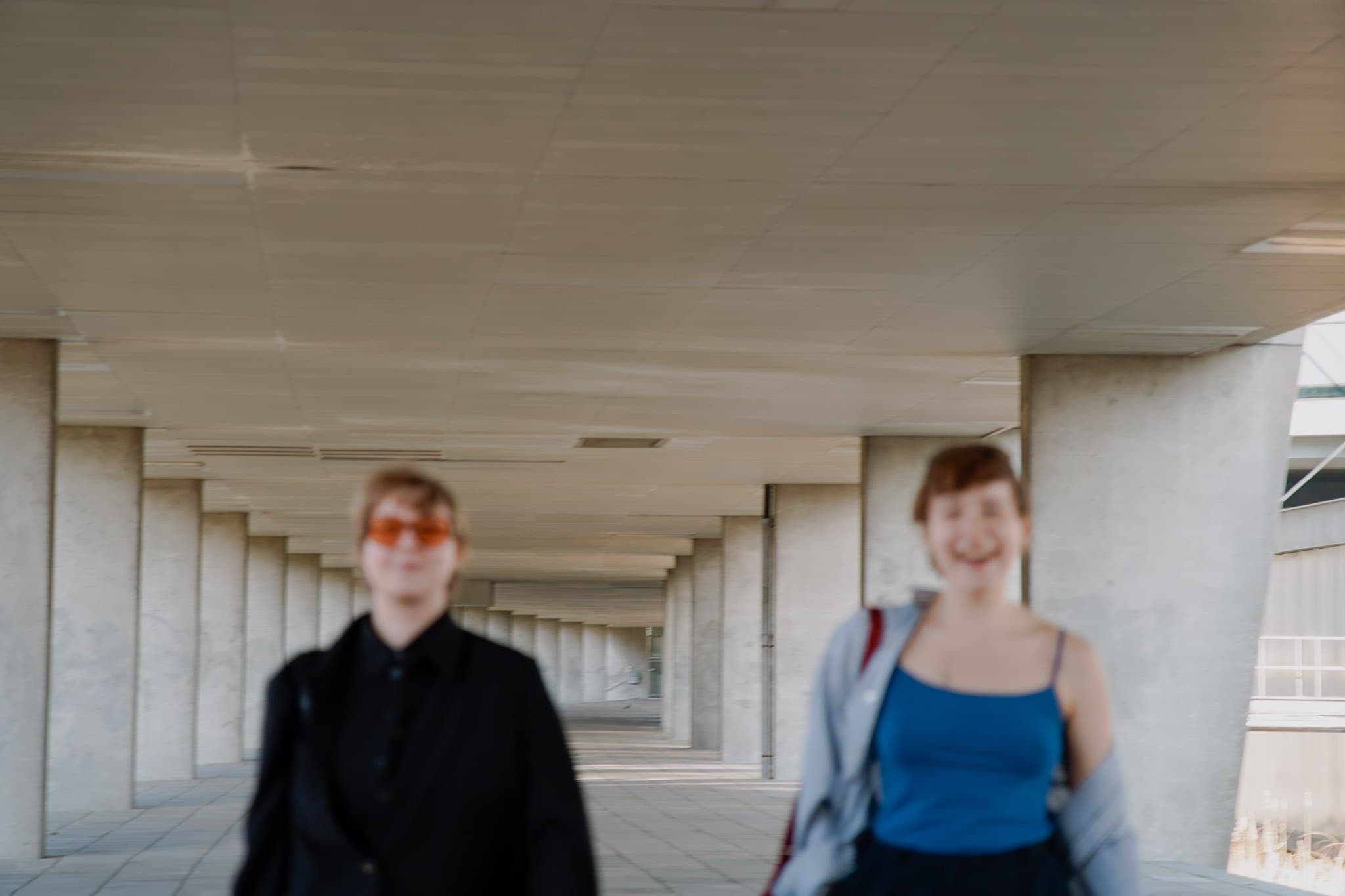 Two people standing in a repeating concrete colonnade.