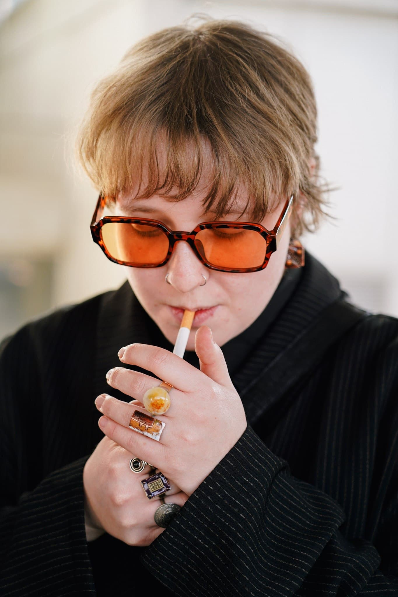 Close-up of a person wearing orange sunglasses and lighting a cigarette.
