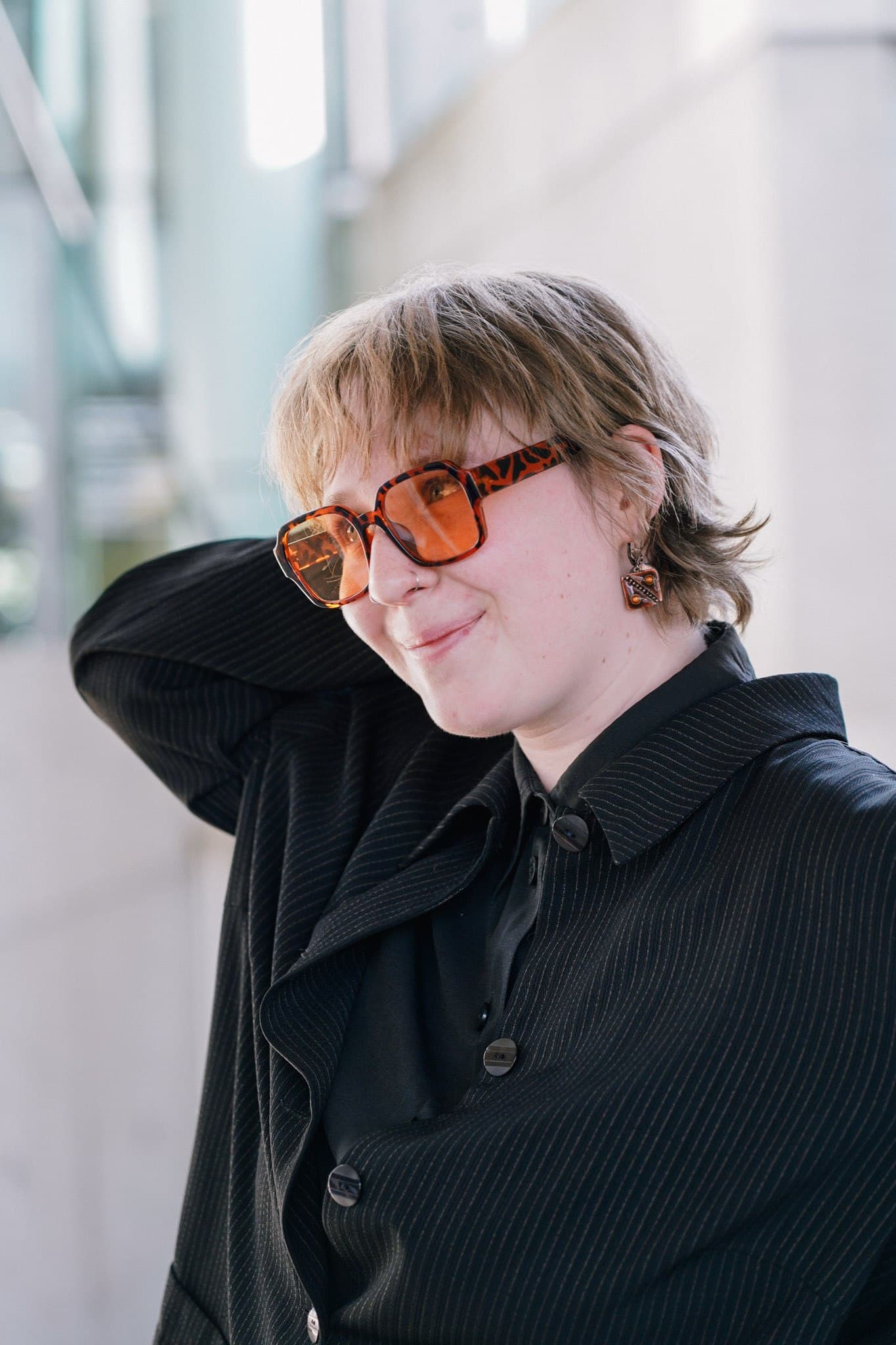 A person wearing orange sunglasses with a hand behind their head.