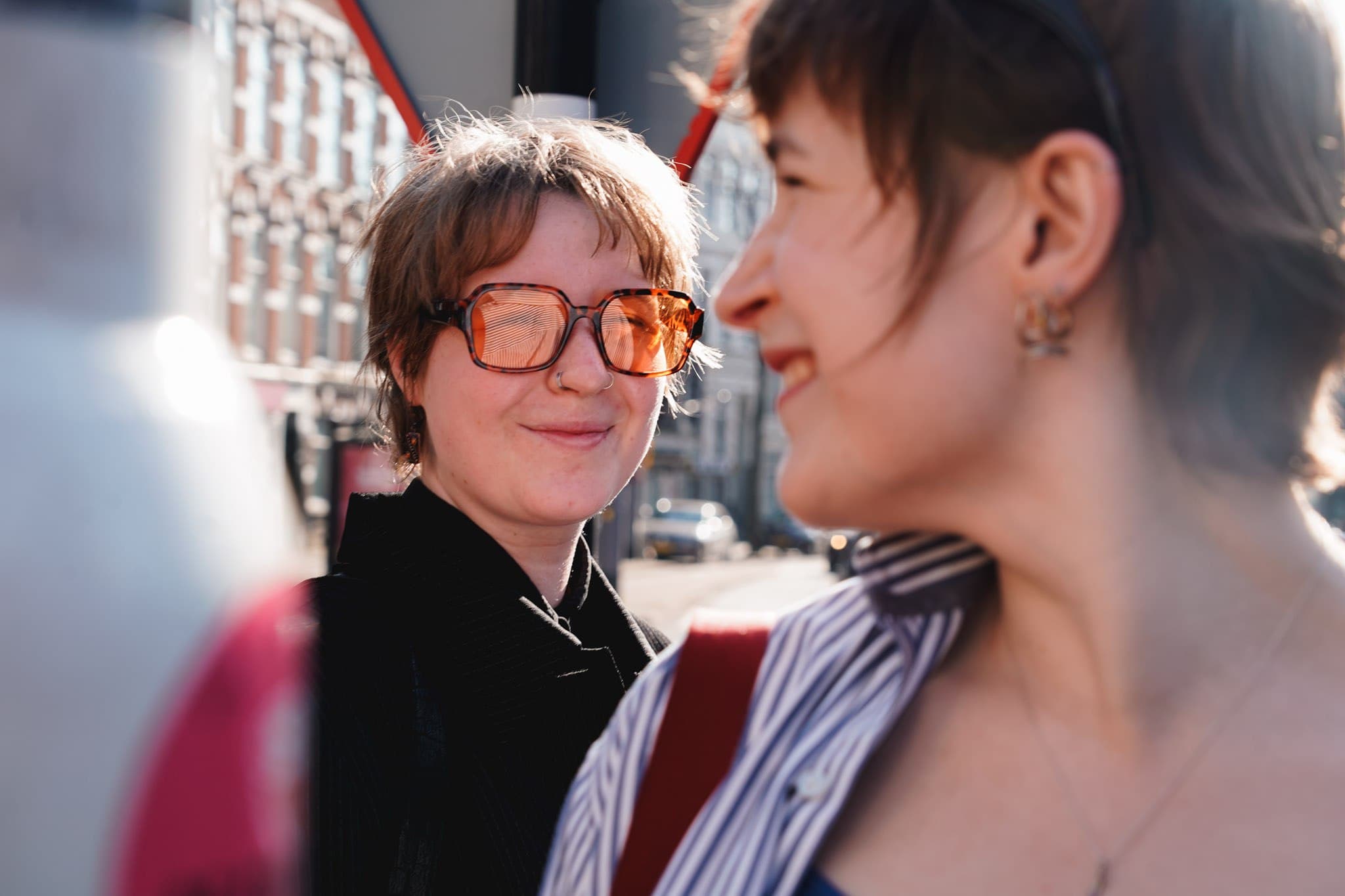 Two people talking on a sunlit city street.