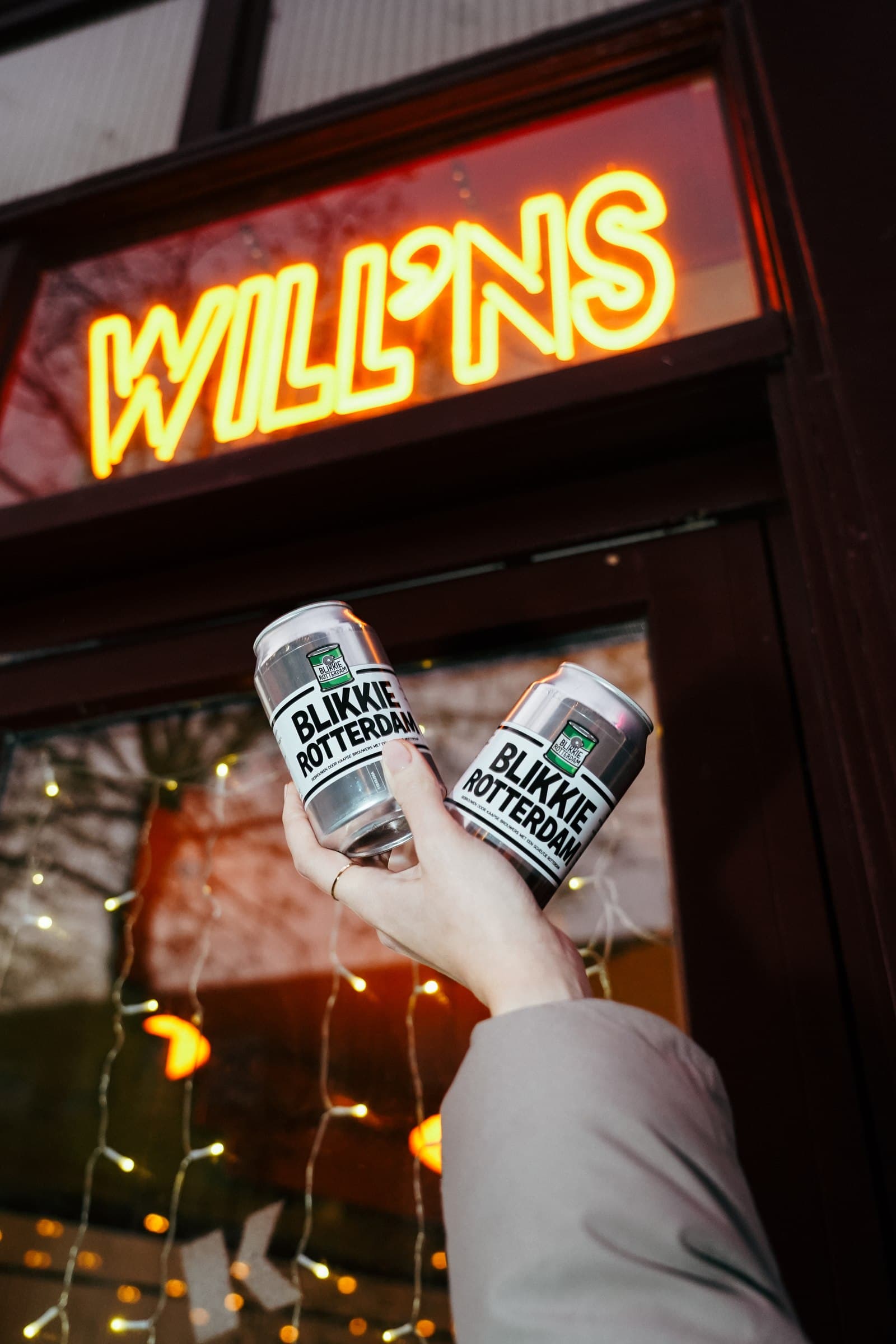 Hands raising drinks beneath an illuminated Will’ns sign.