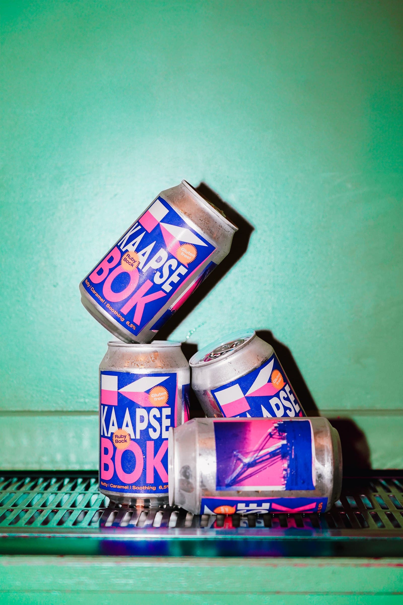Kaapse Bok cans balanced in a sculptural arrangement against a green background.