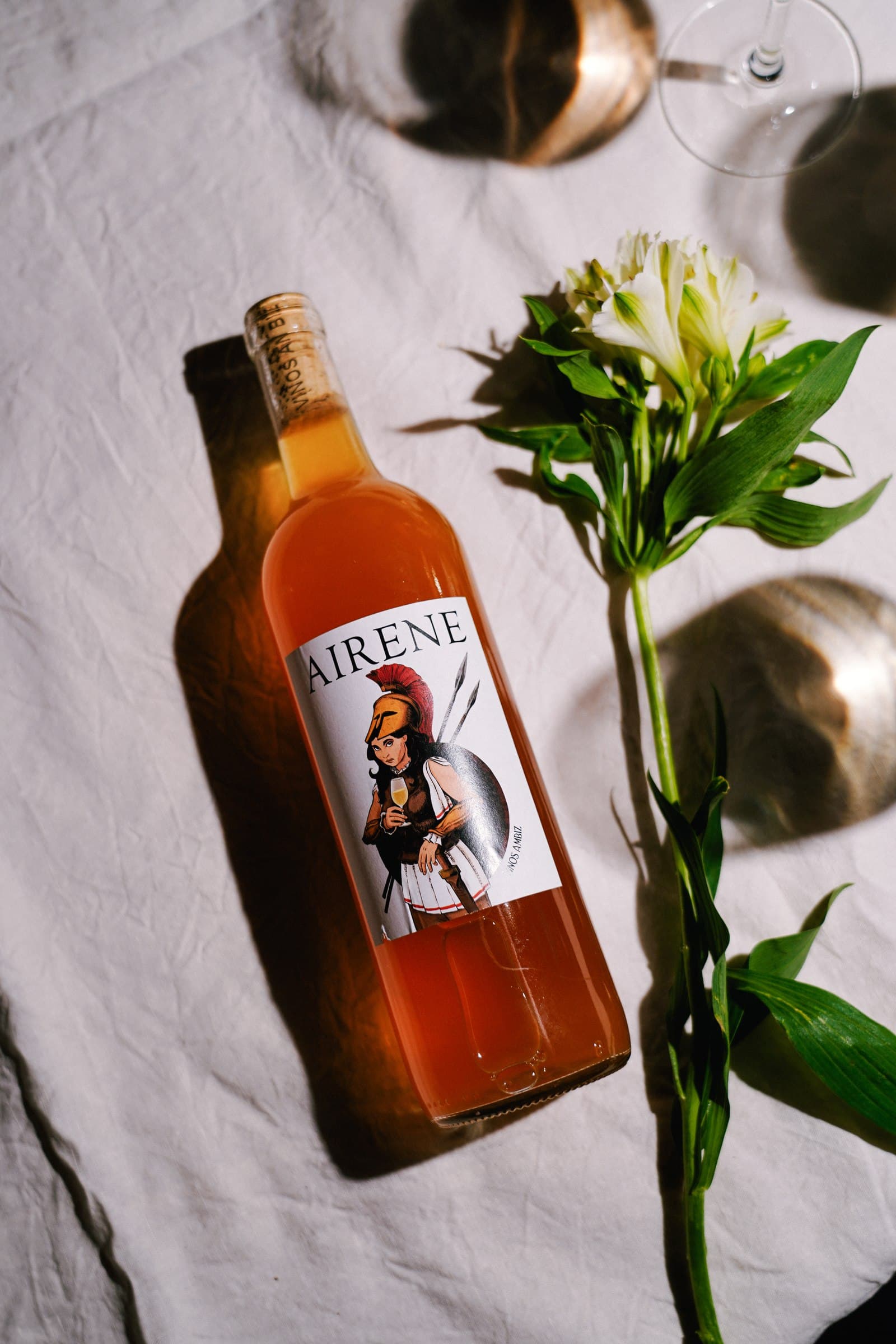 An amber drinks bottle and a glass beside green stems on a white surface.