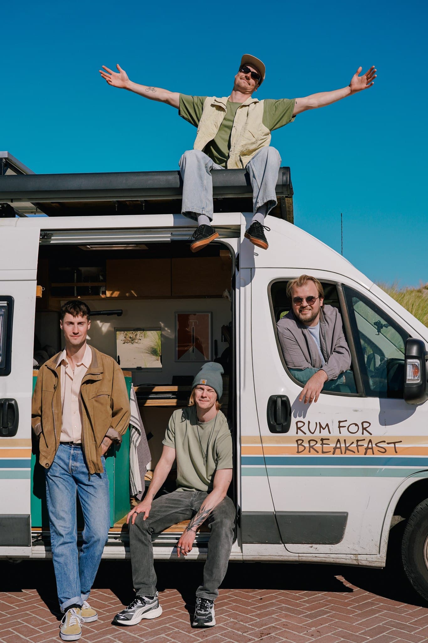 Rum for Breakfast posing in and on a white campervan with the band name painted on its side.