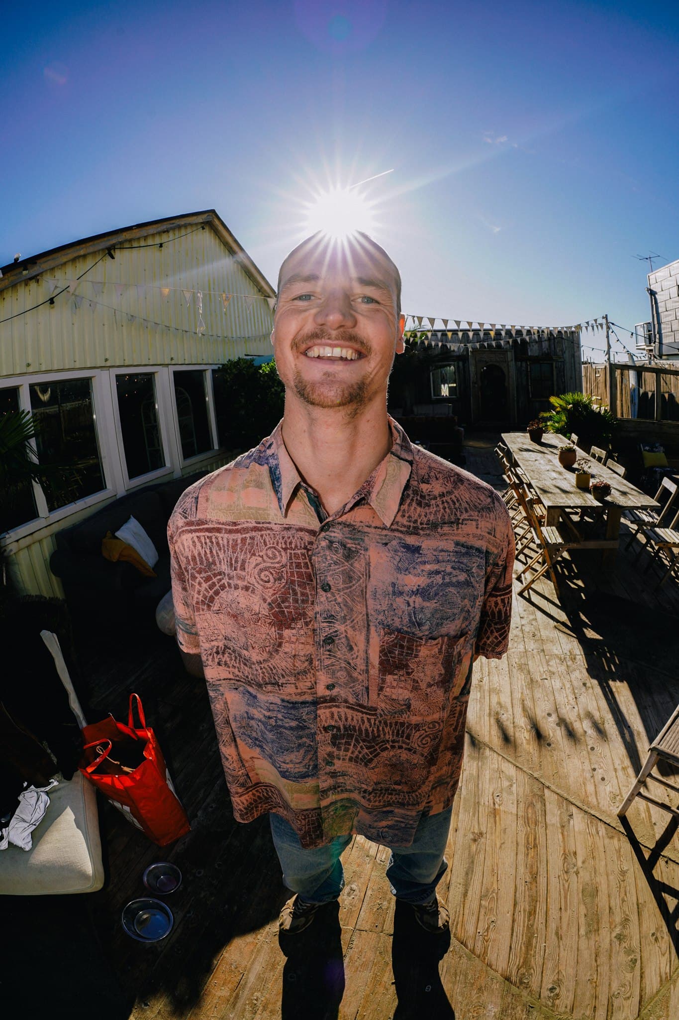 A band member smiling on a sunny wooden terrace, with the sun above his head.