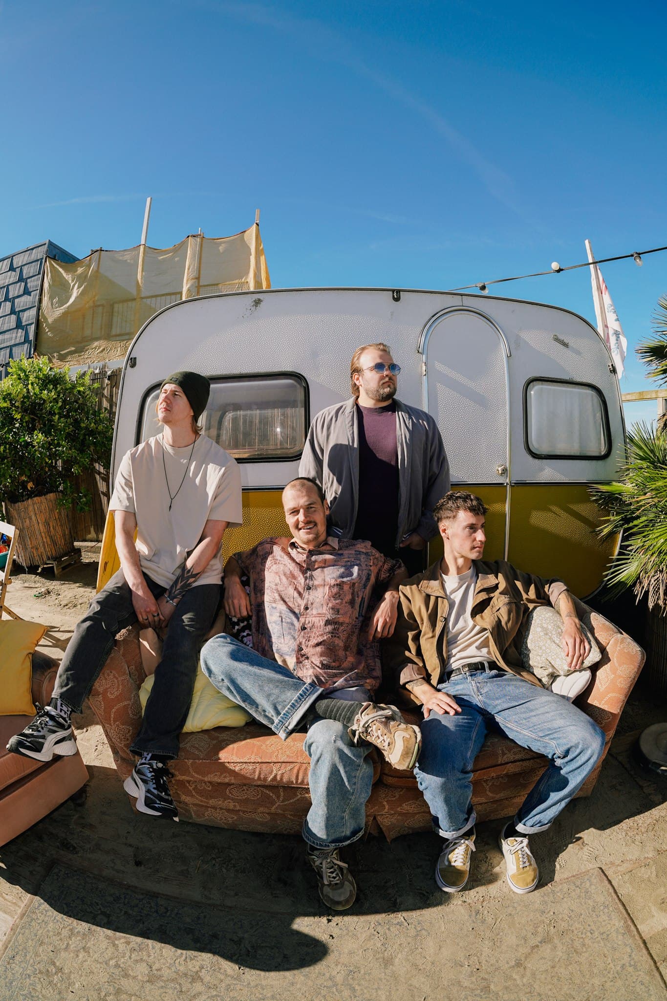 Four Rum for Breakfast band members posing on and behind a sofa in front of a caravan.
