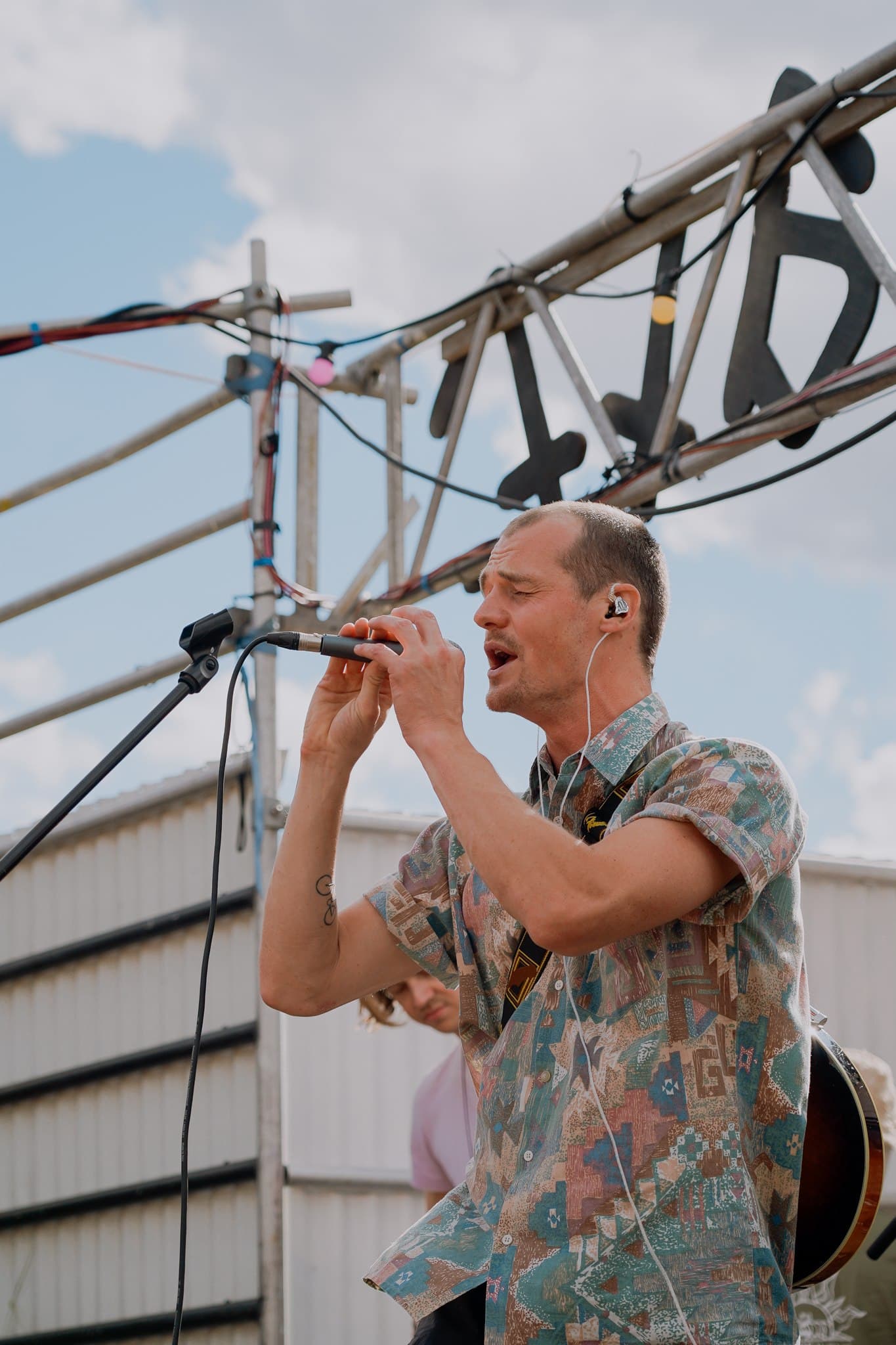 A musician singing into a microphone during an outdoor performance.