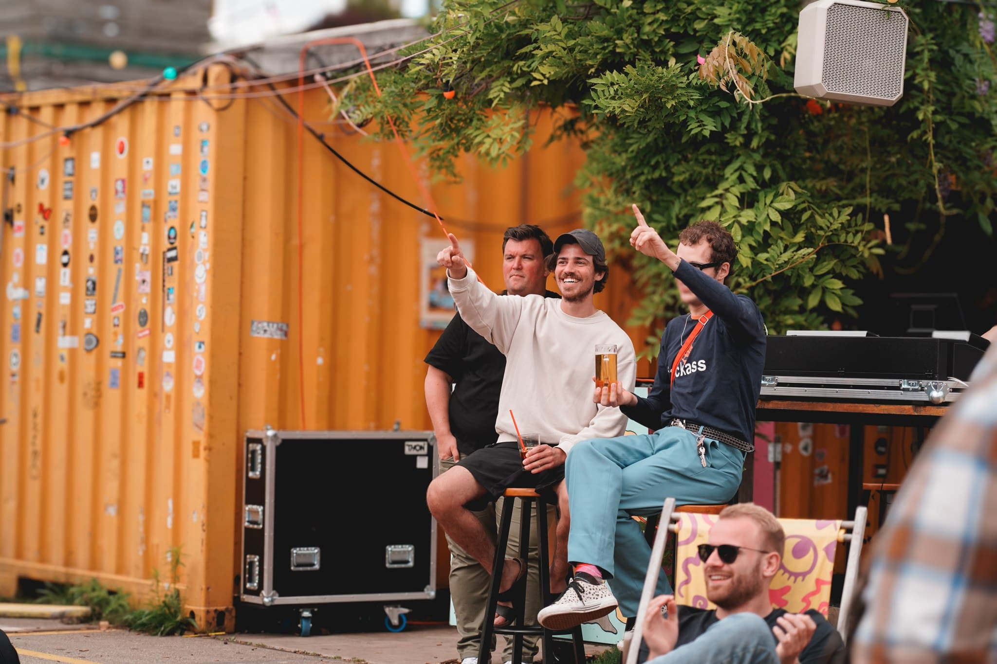 Band members beside an orange shipping container and musical equipment.