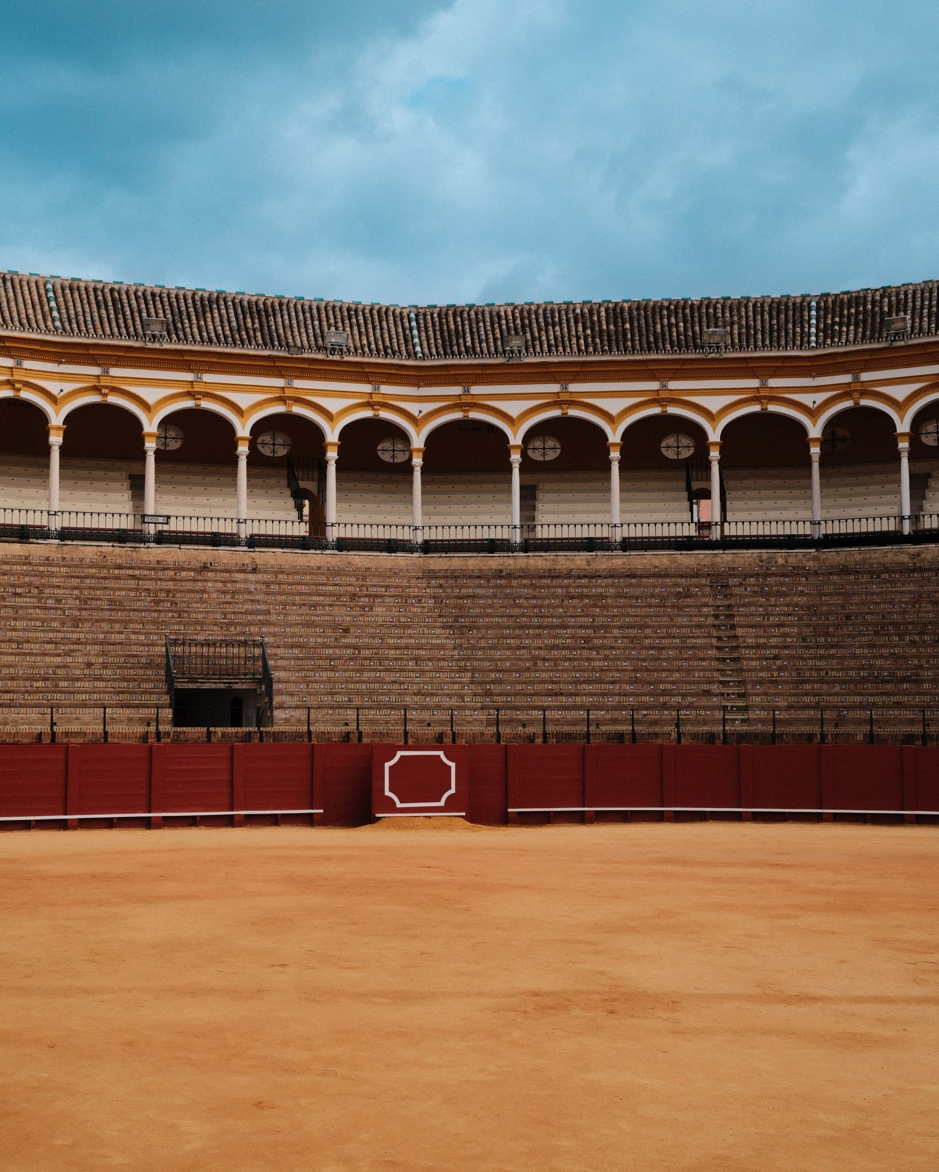 Empty bullring with tiered seating and arched galleries.