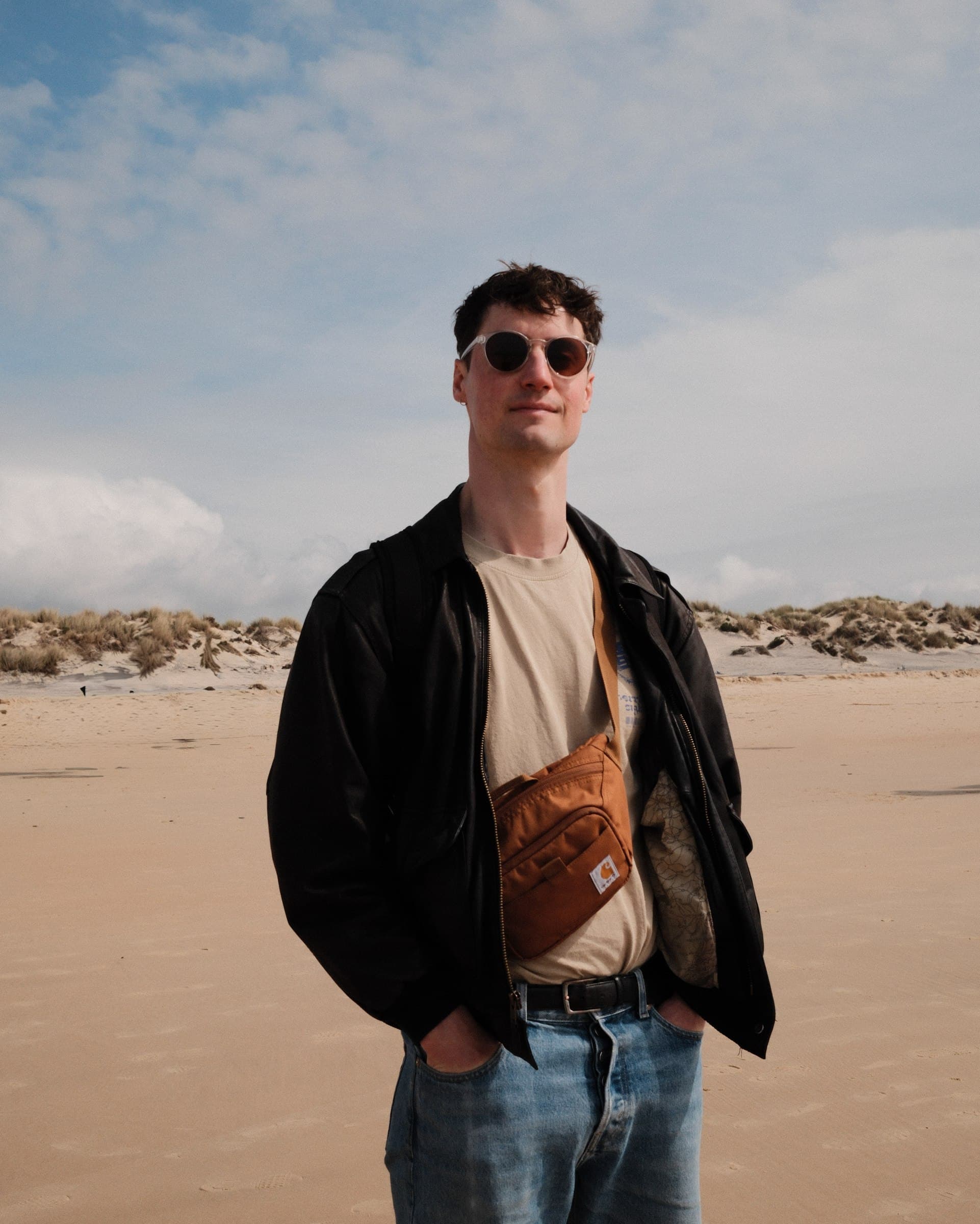 Portrait on a broad sandy beach beneath a cloudy sky.