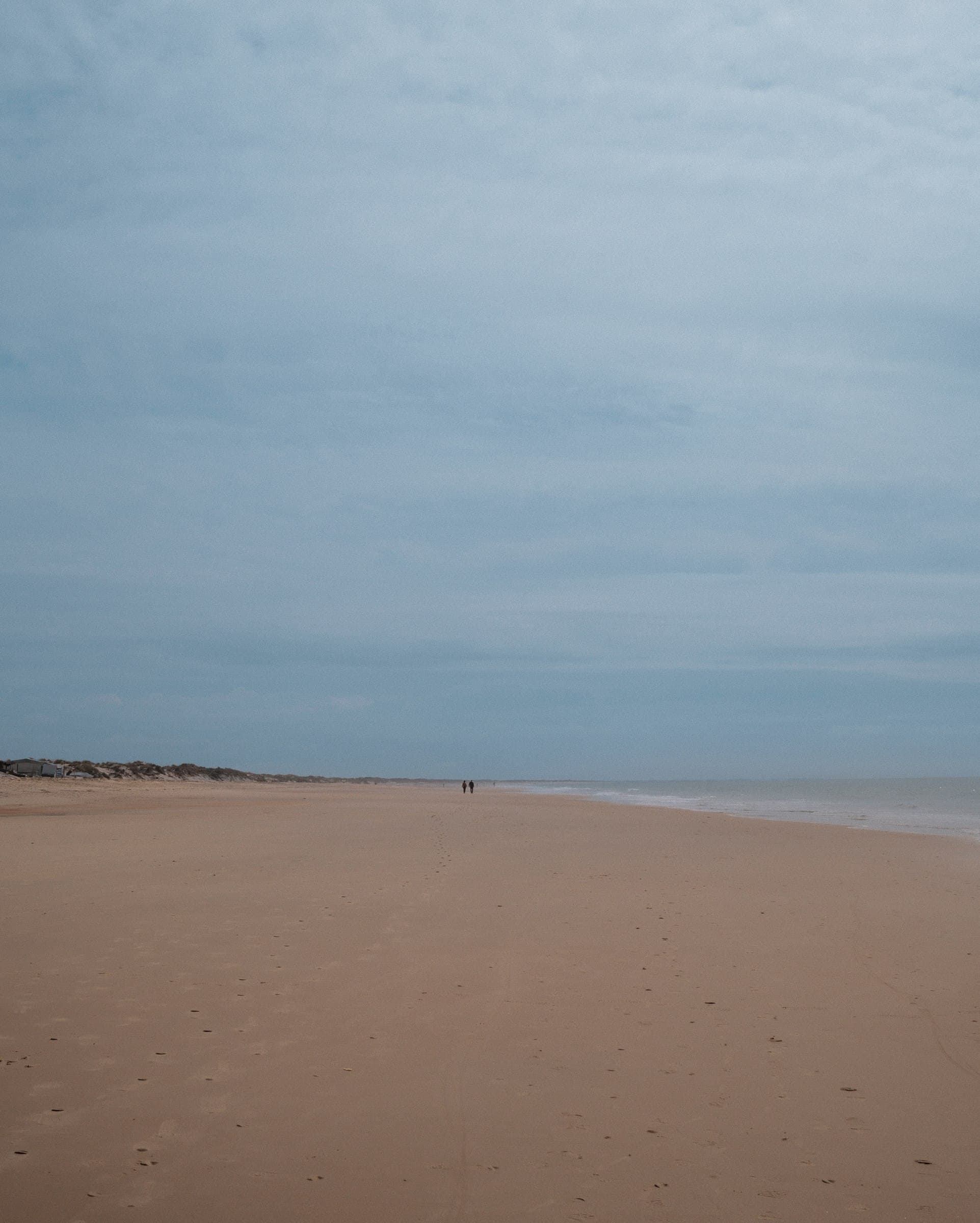 An expansive beach and calm sea beneath a pale sky.