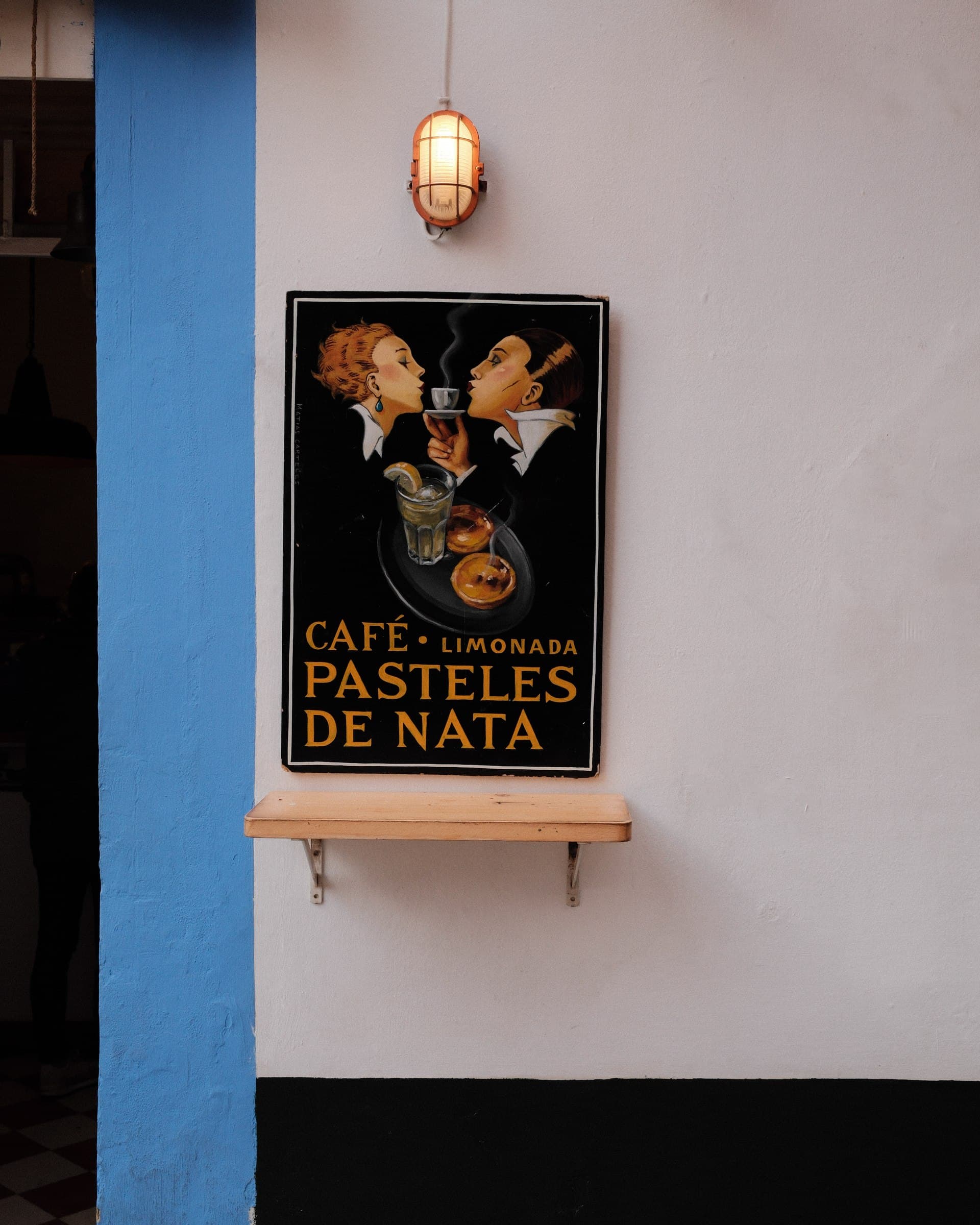 A small pastry shop sign on a pale wall beside a blue doorway.