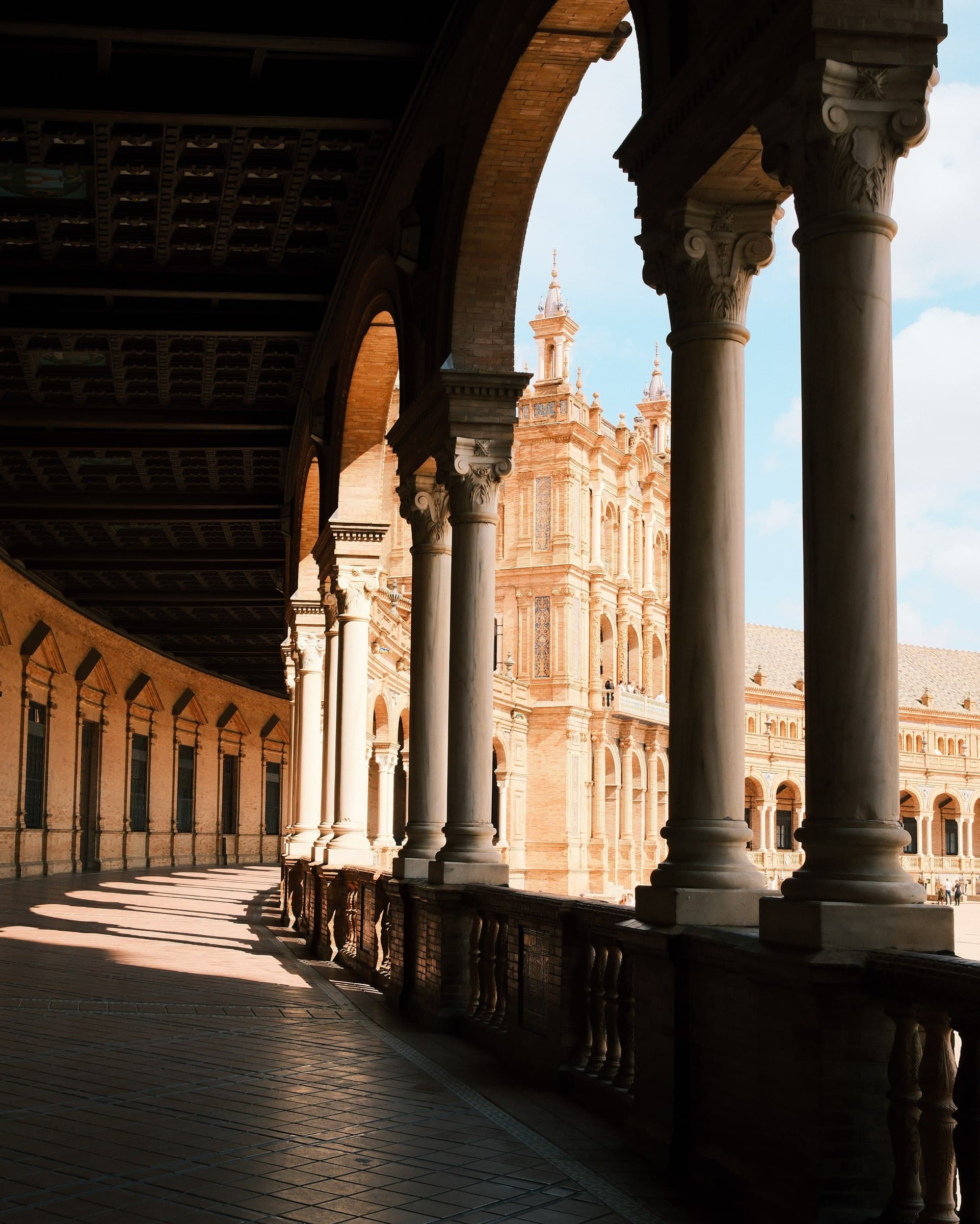 A shaded arcade opening onto sunlit historic architecture.