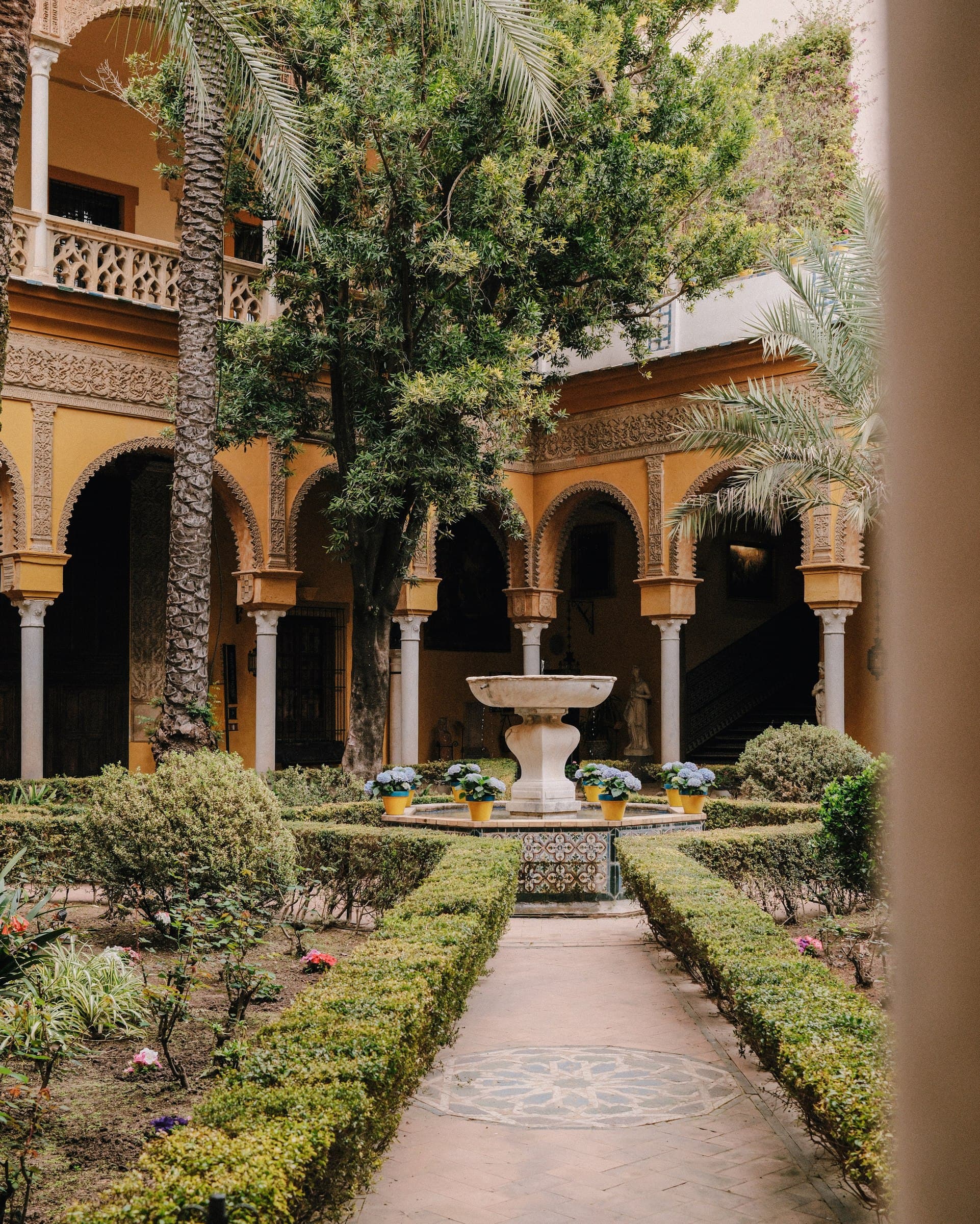 A planted courtyard with arches, hedges and a central fountain.