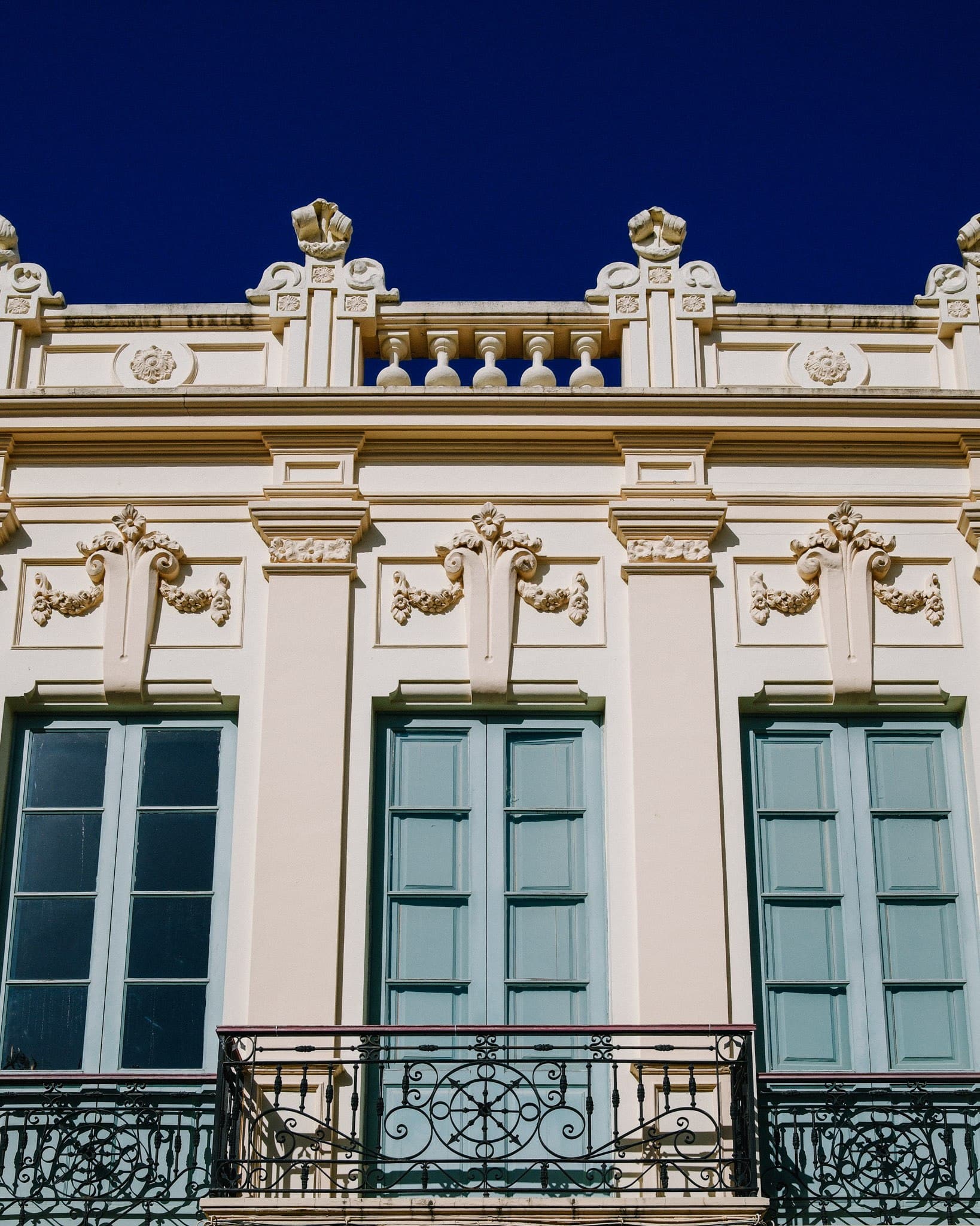 Ornate cream-coloured building facade with green shutters and balconies.