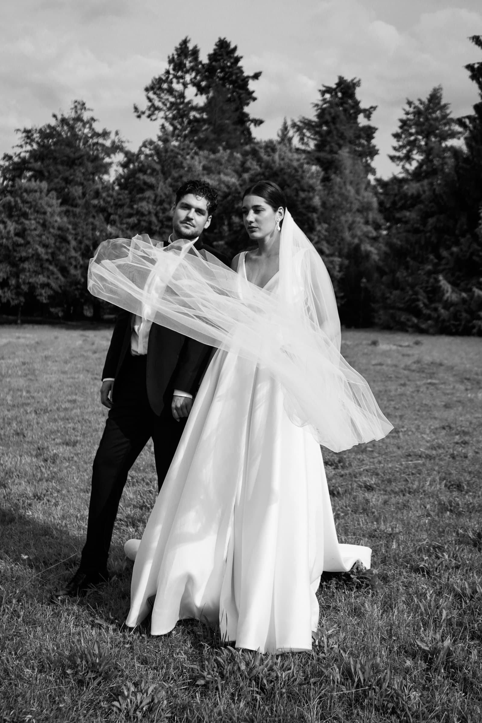 The wedding couple embracing outdoors beneath the bride’s veil in black and white.