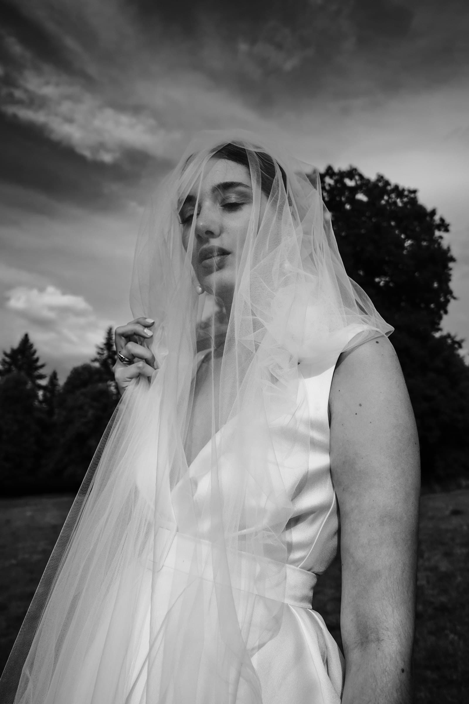 The bride holding her veil in a black-and-white outdoor portrait.