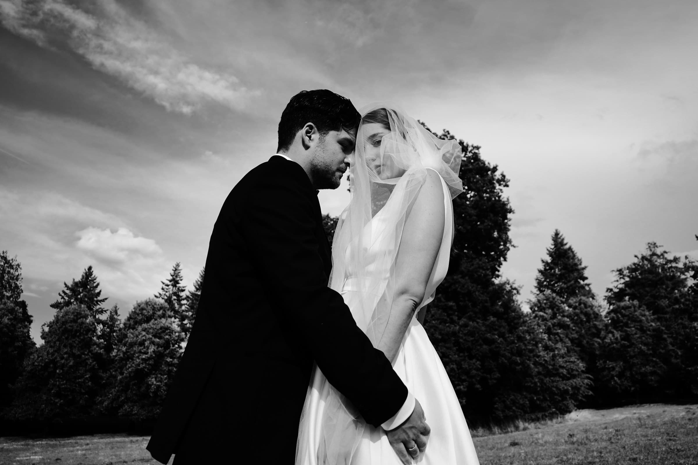 Black-and-white photograph of the wedding couple kissing beneath the veil.
