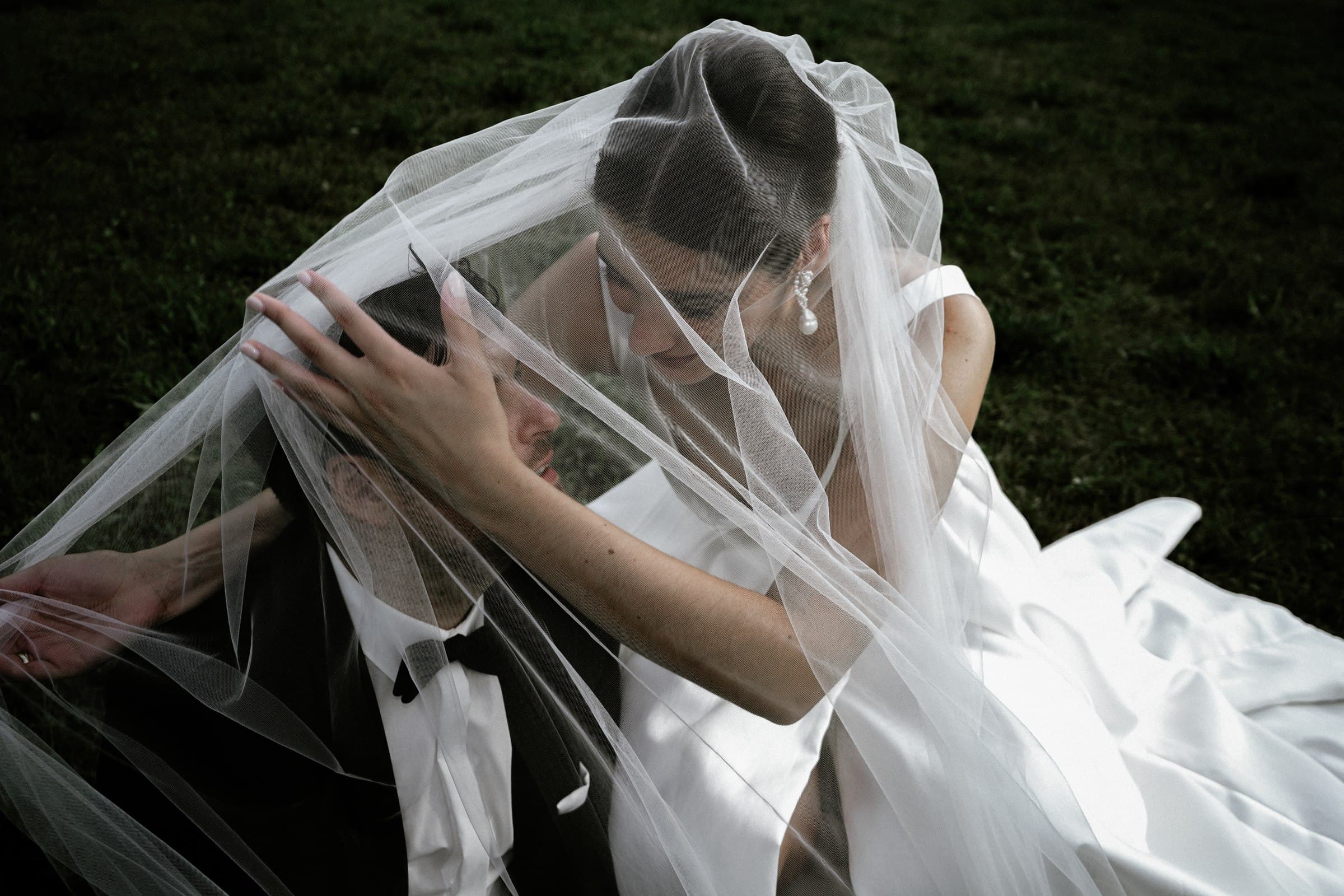 Close-up of the wedding couple embracing beneath a translucent veil.