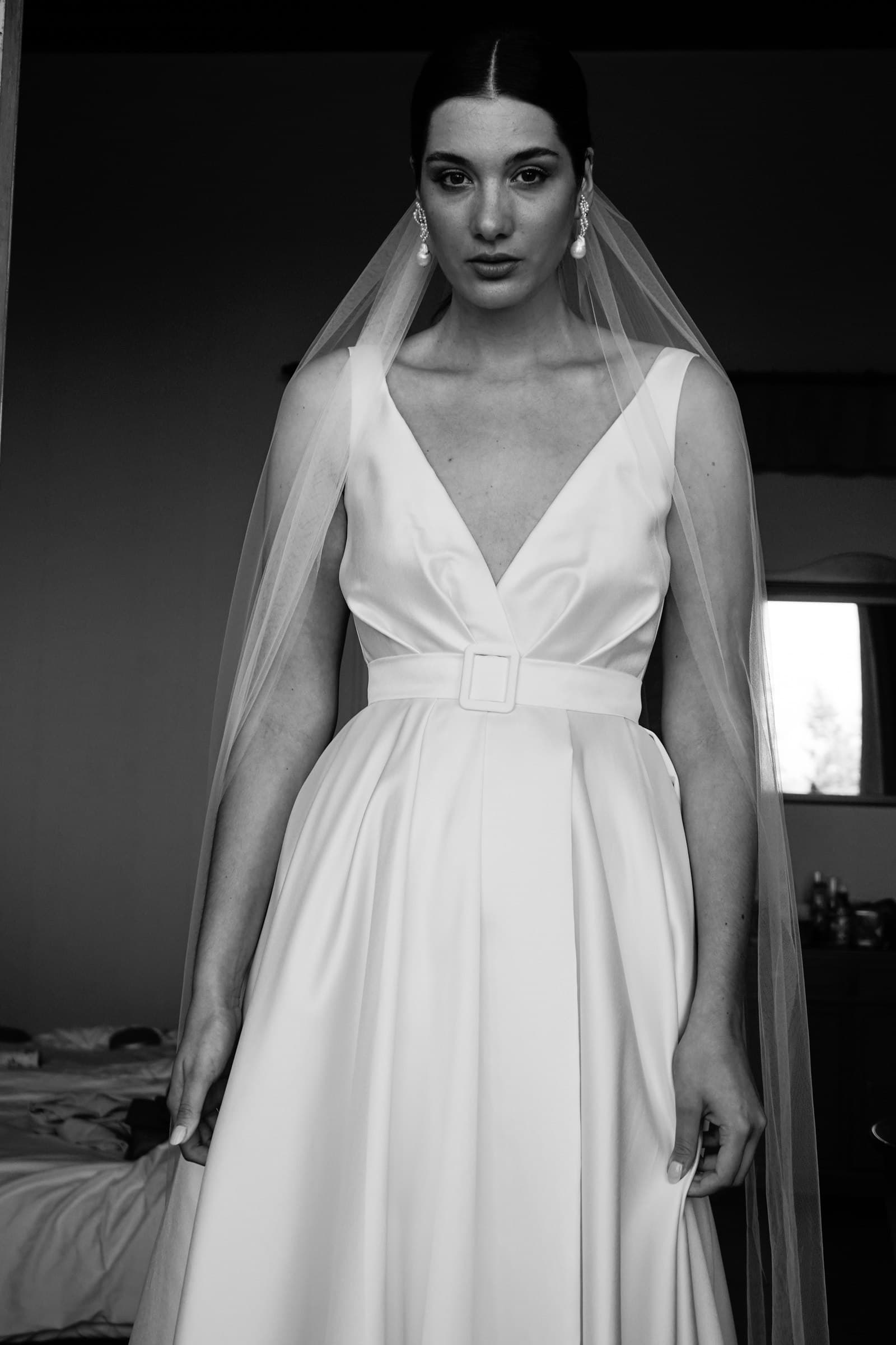 The bride standing in a doorway wearing her wedding dress, in black and white.