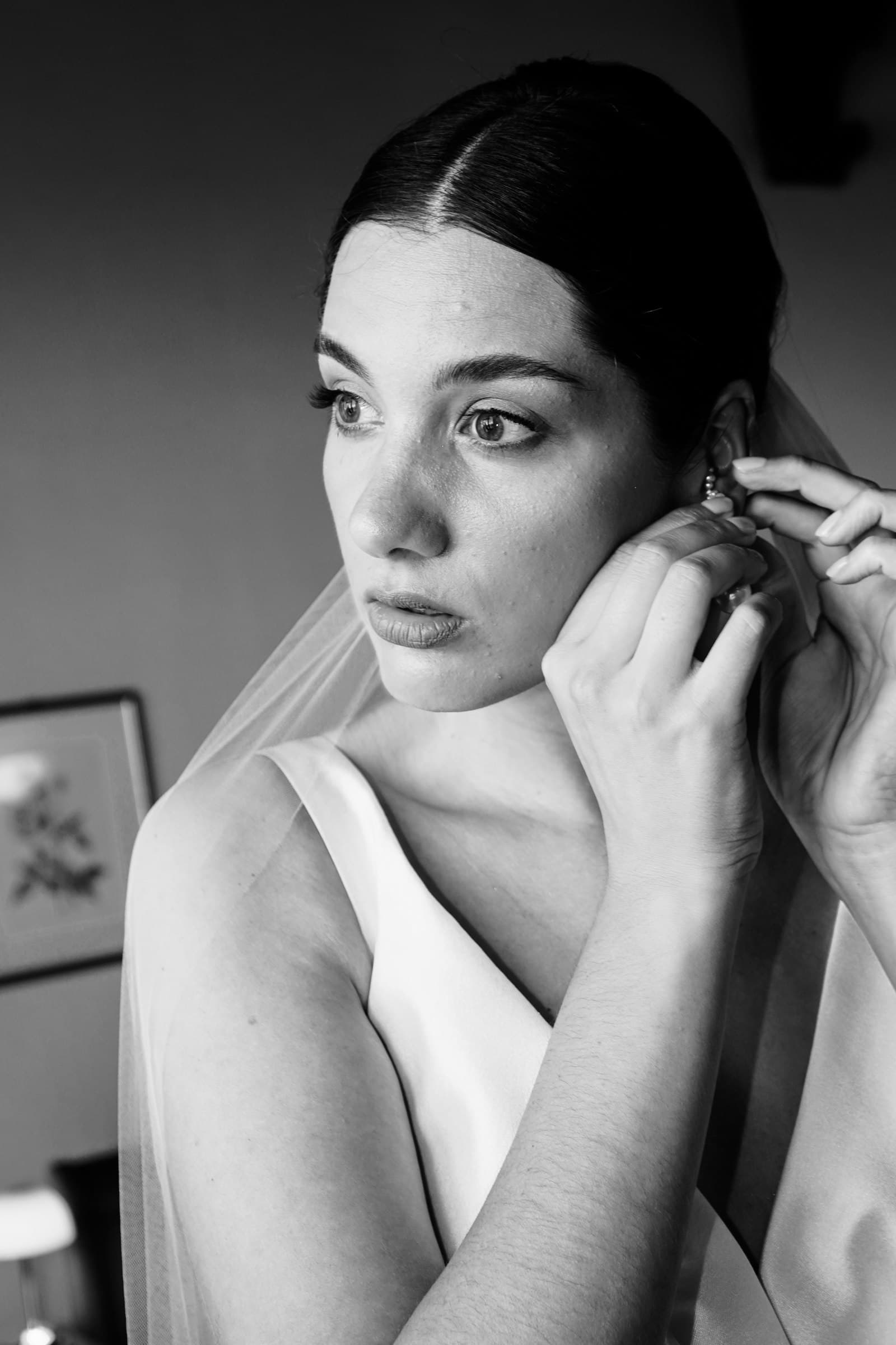 Black-and-white close-up of the bride adjusting an earring.